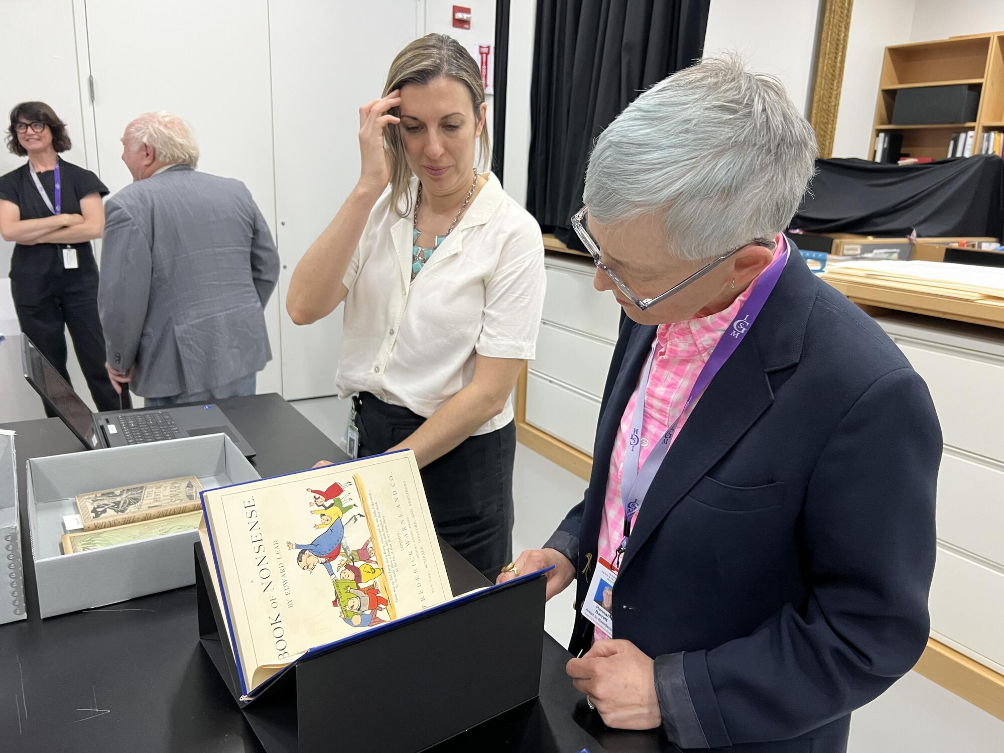 Woman with short grey hair looking through a book sitting next to another woman