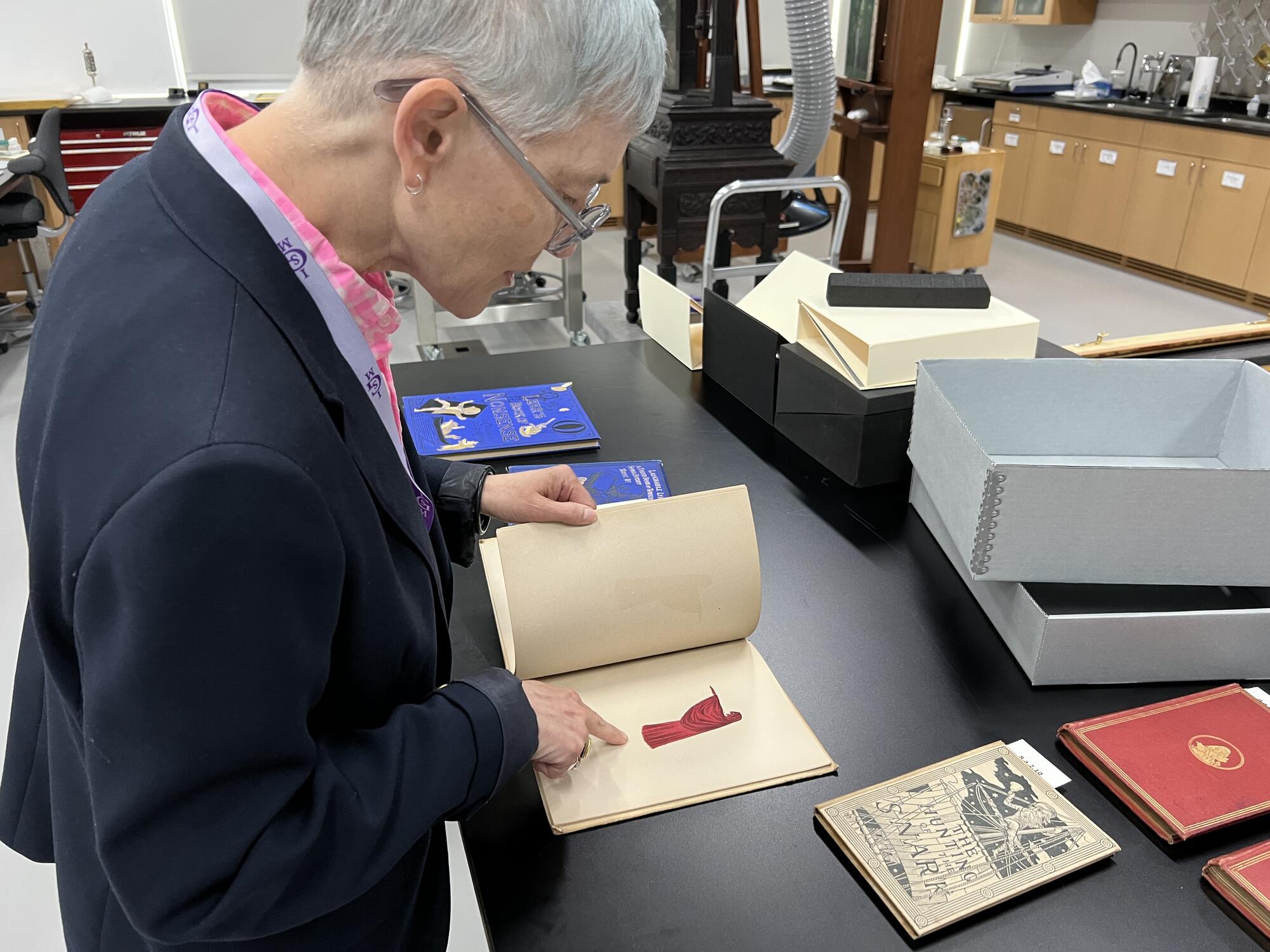 Woman with short grey hair looking at a book on top of a high counter. 
