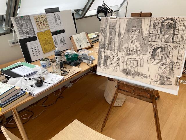 A table and easel filled with sketches in a sunny studio space