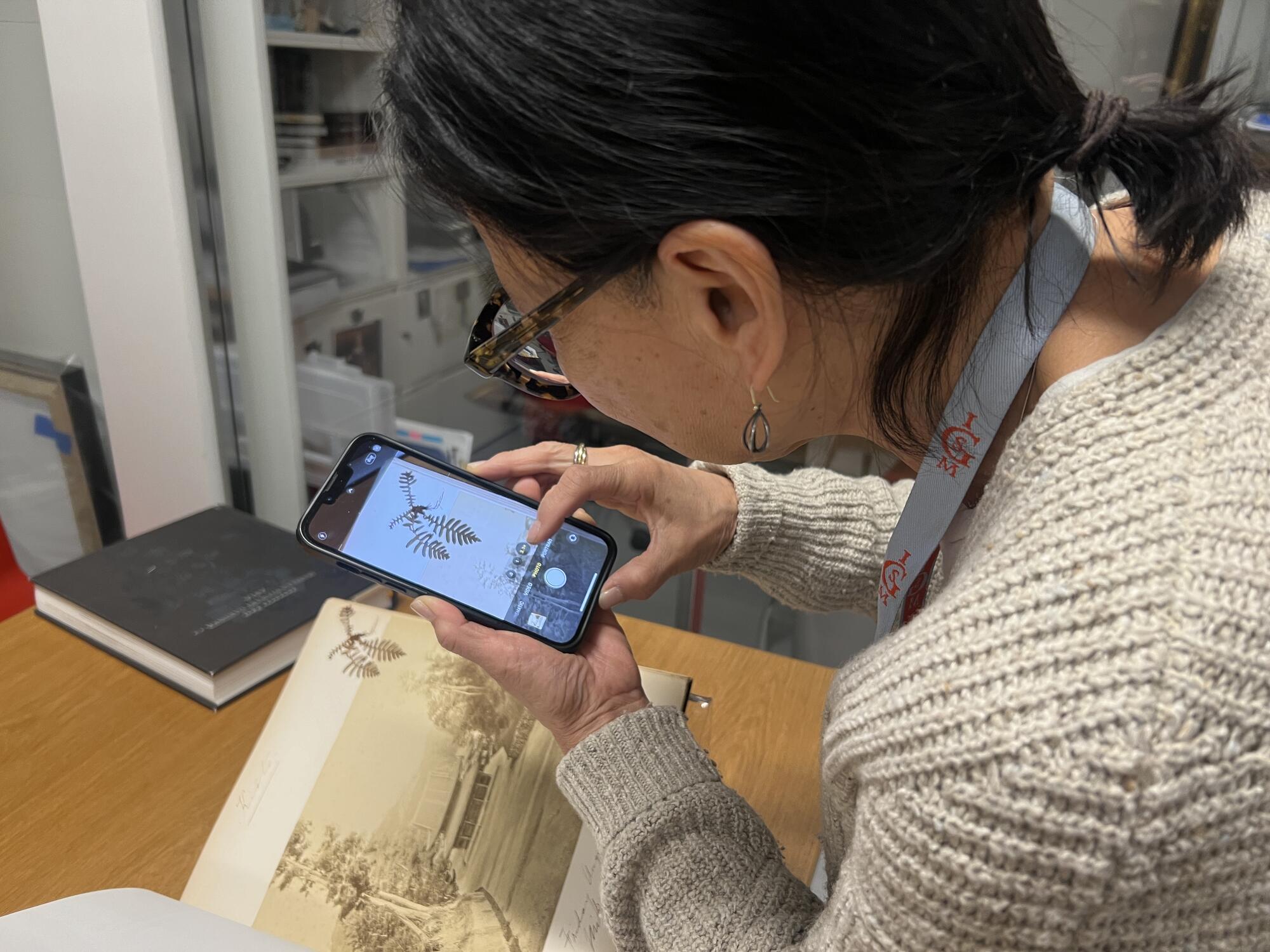 A woman photographing a page of a scrapbook on a smart phone. 