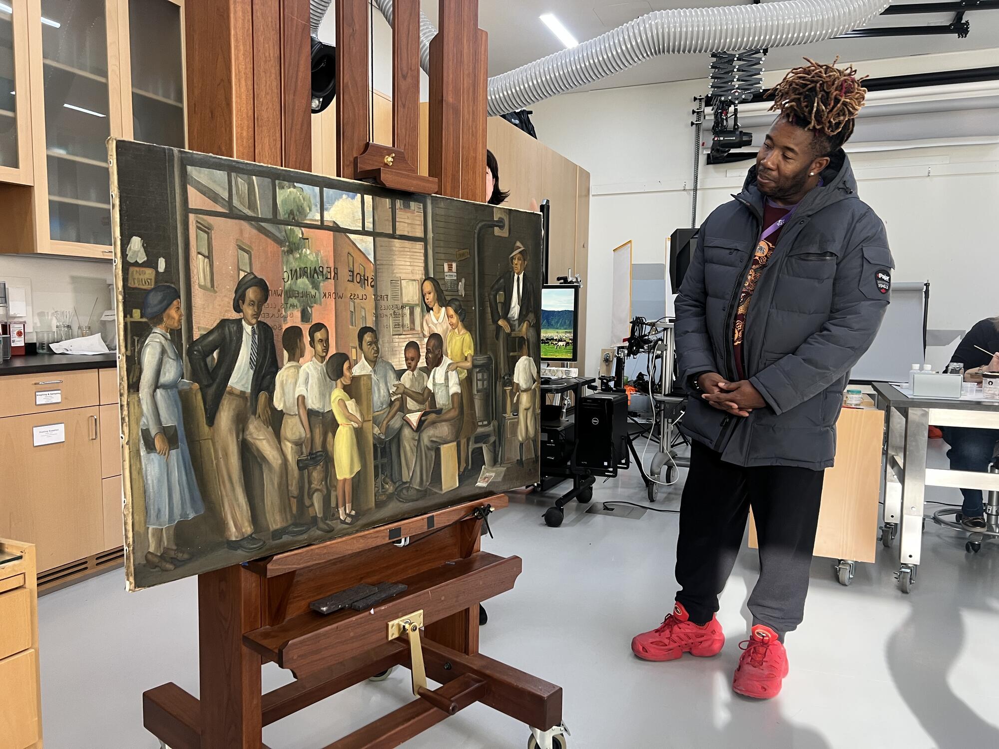 An African American man wearing a winter jacket examining a painting in a laboratory setting. 