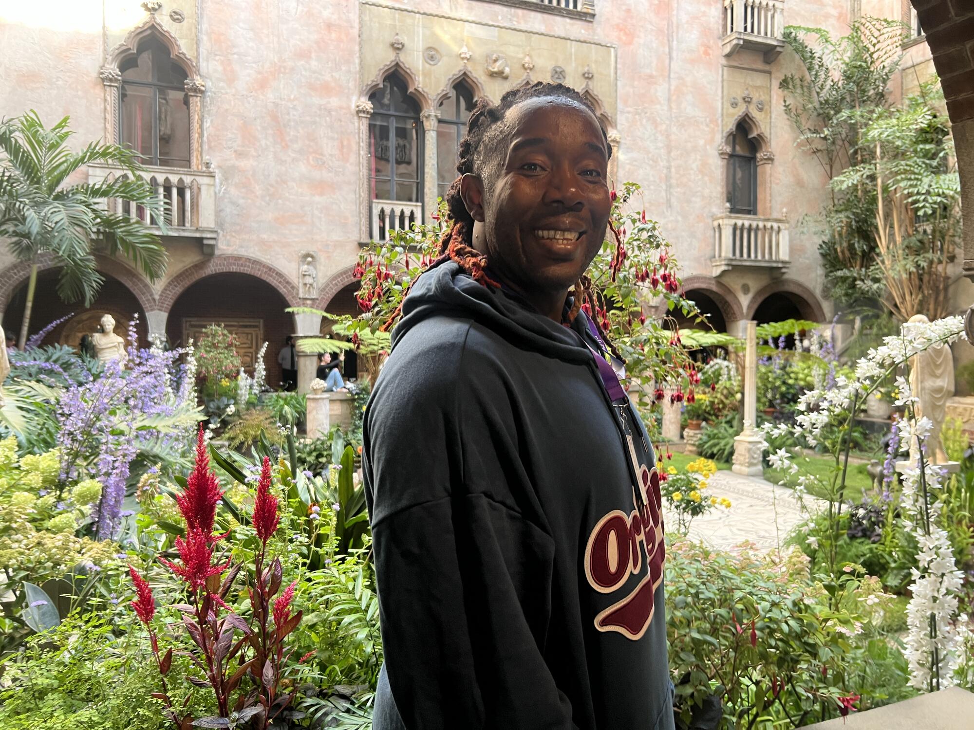 An African American man with braids pulled back on his head looks directly at the camera, smiling. 