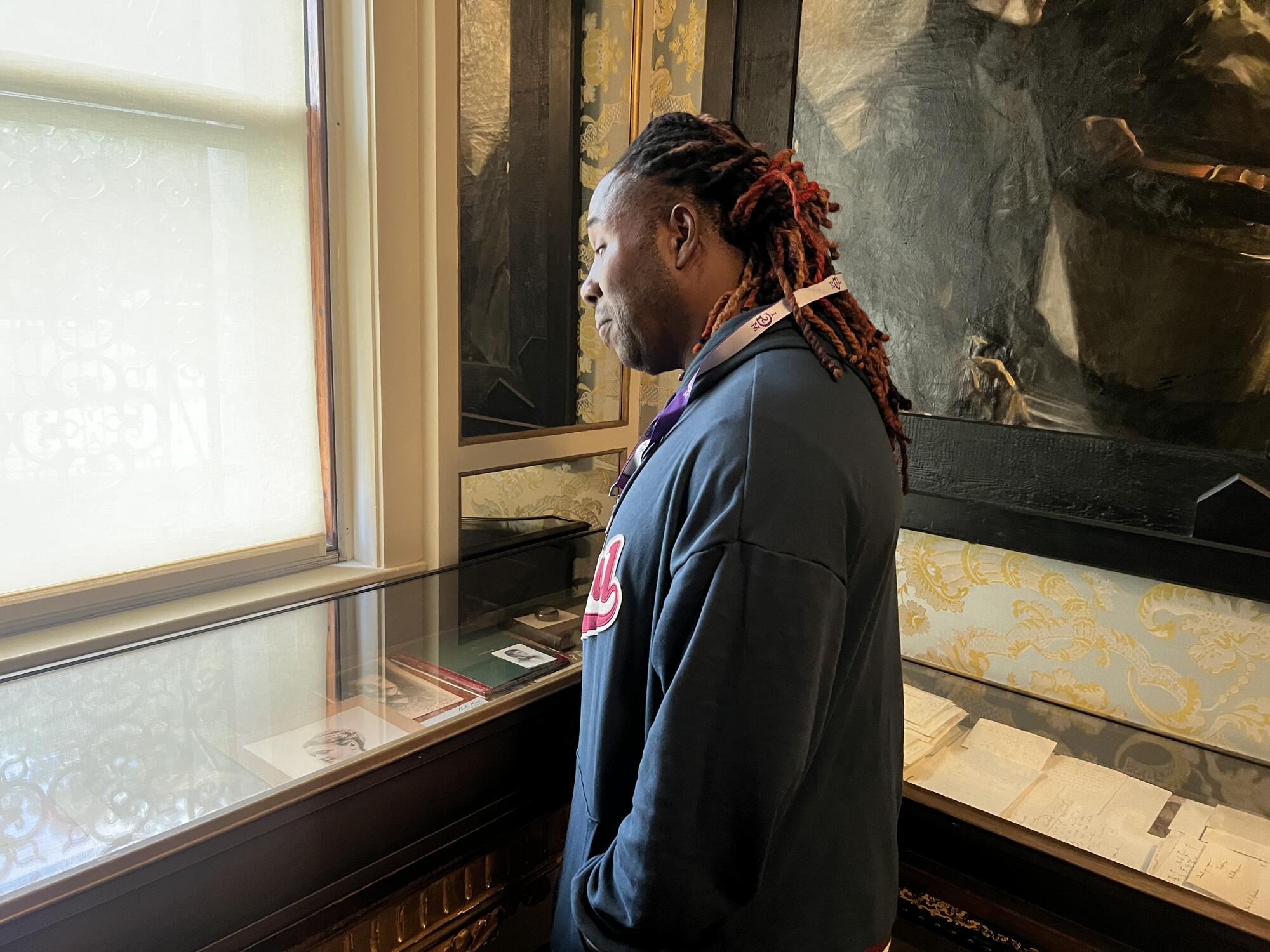 An African American man with braids pulled back looking down into a glass case with art objects inside. 