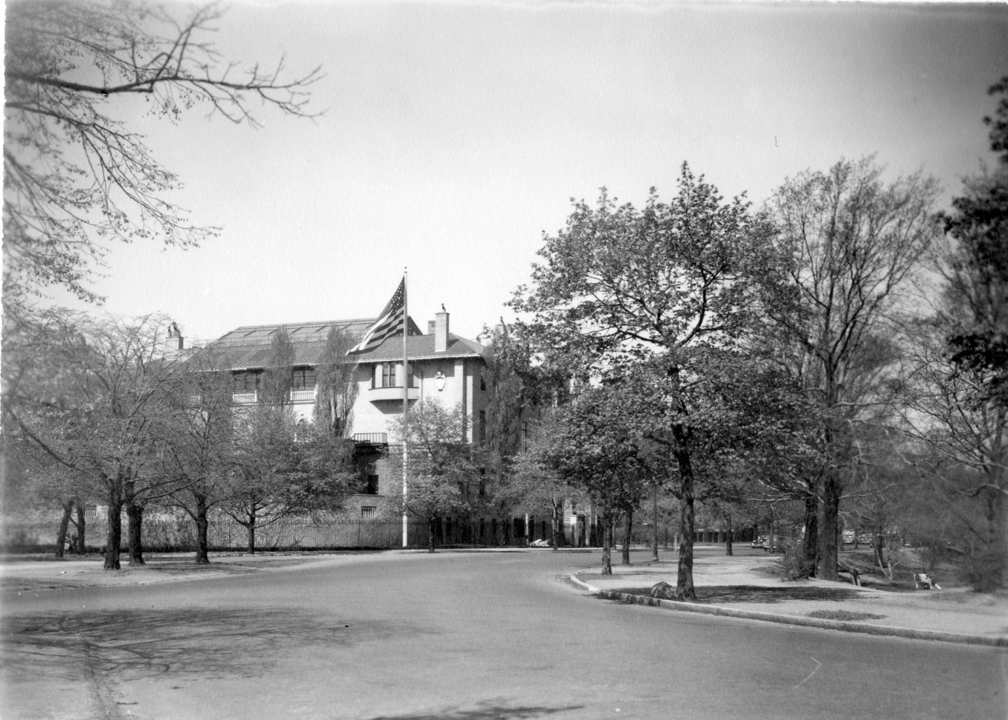 Black and white photograph of the museum with a tree-lined road in the foreground and an American flag flying on a flag pole in front of the museum