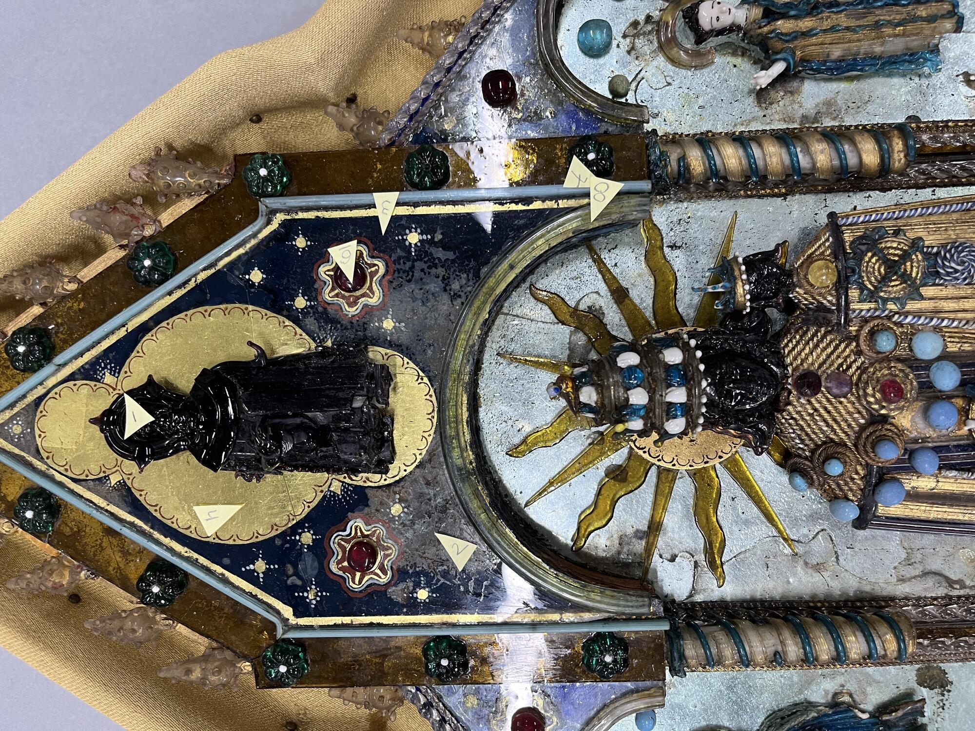 A close-up photo of the Black Glass Madonna showing small yellow paper triangles throughout.