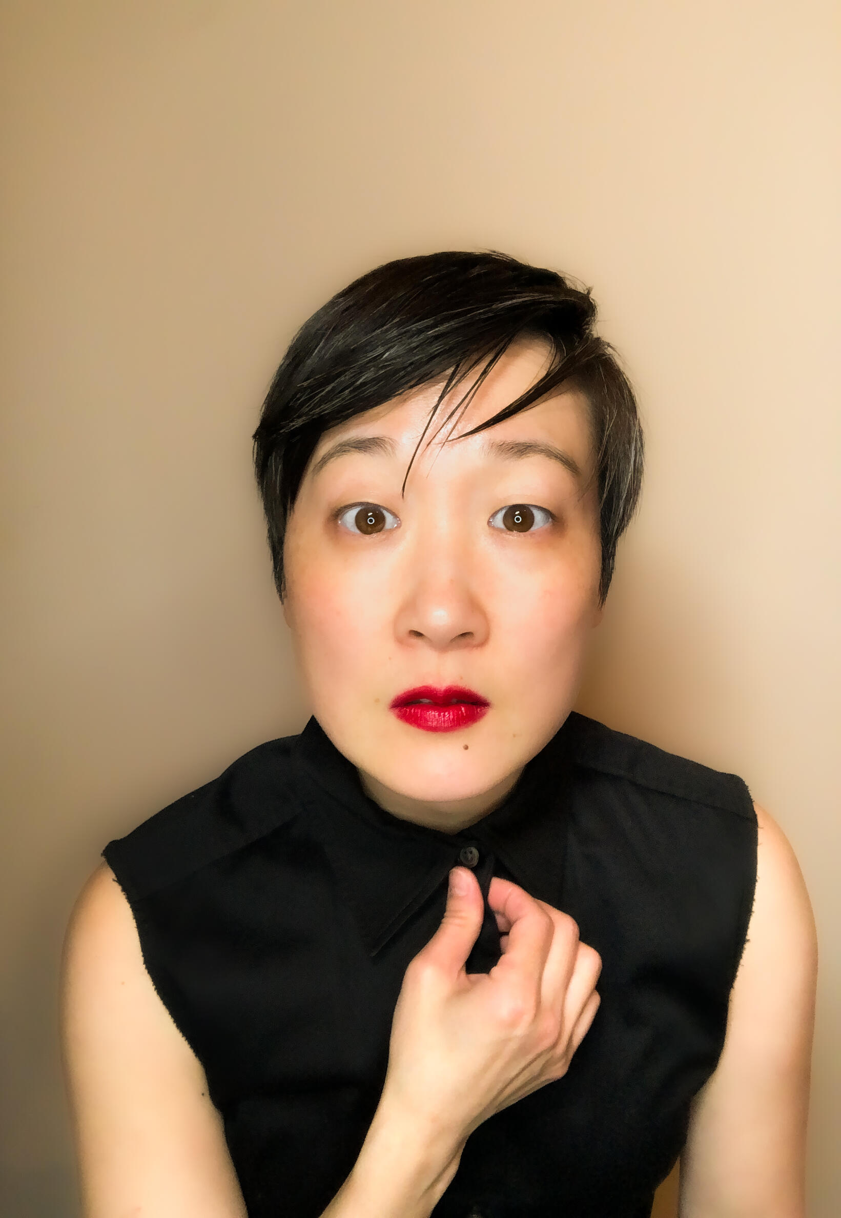 Young Asian woman with short dark hair, pale skin wearing a black sleeveless top and bright red lipstick looking directly at the camera 