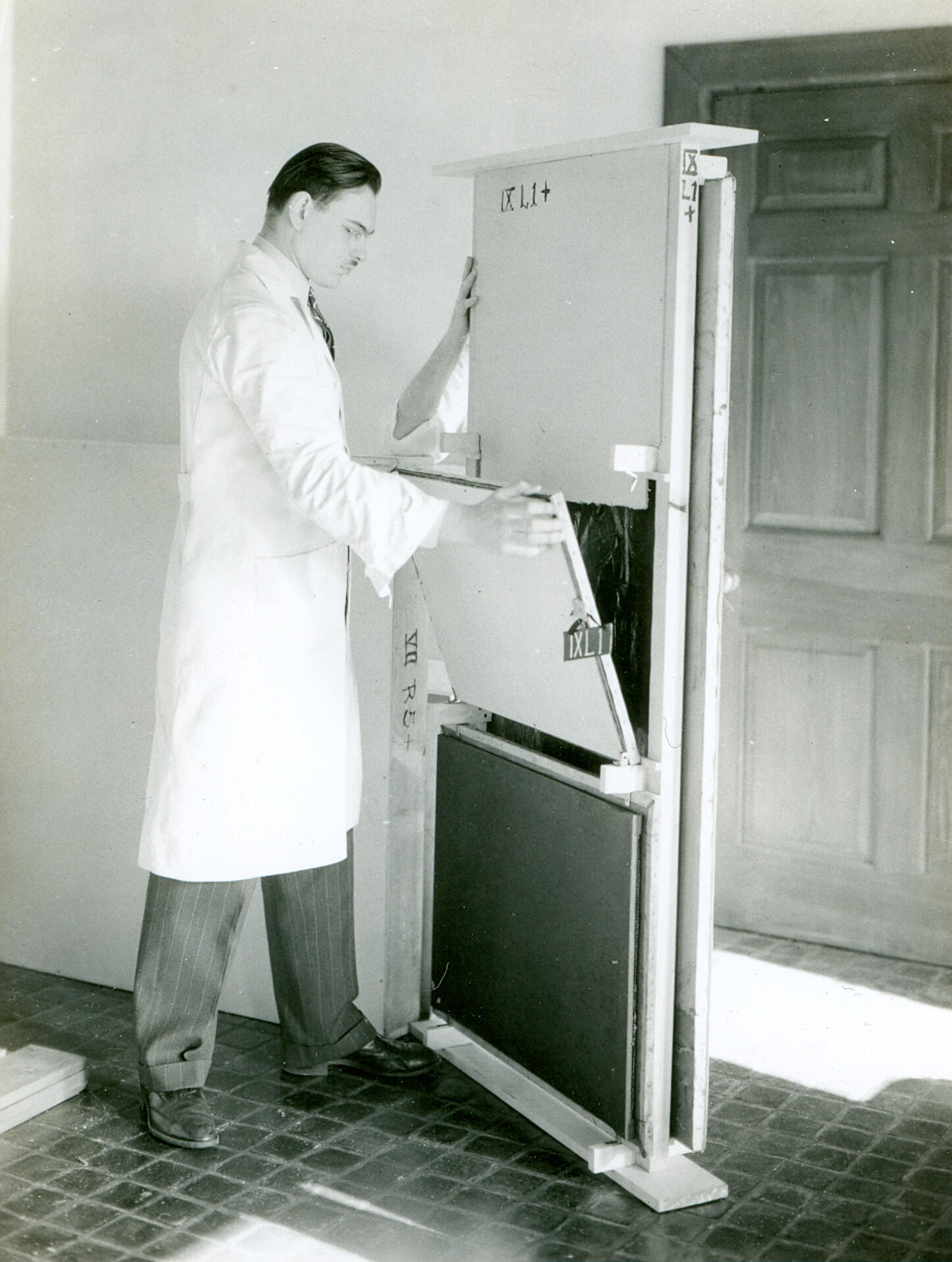 A man standing in a white lab coat loading packed paintings onto a wooden easel that holds multiple paintings