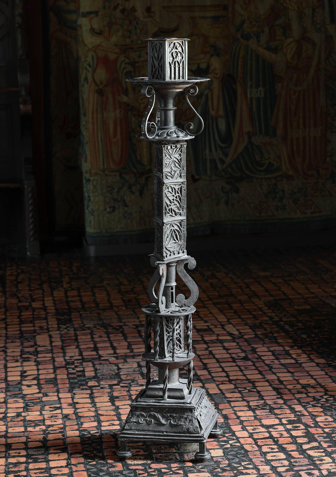 A black iron standing candlestick with socket holder, decorated with panels of foliate patterns.