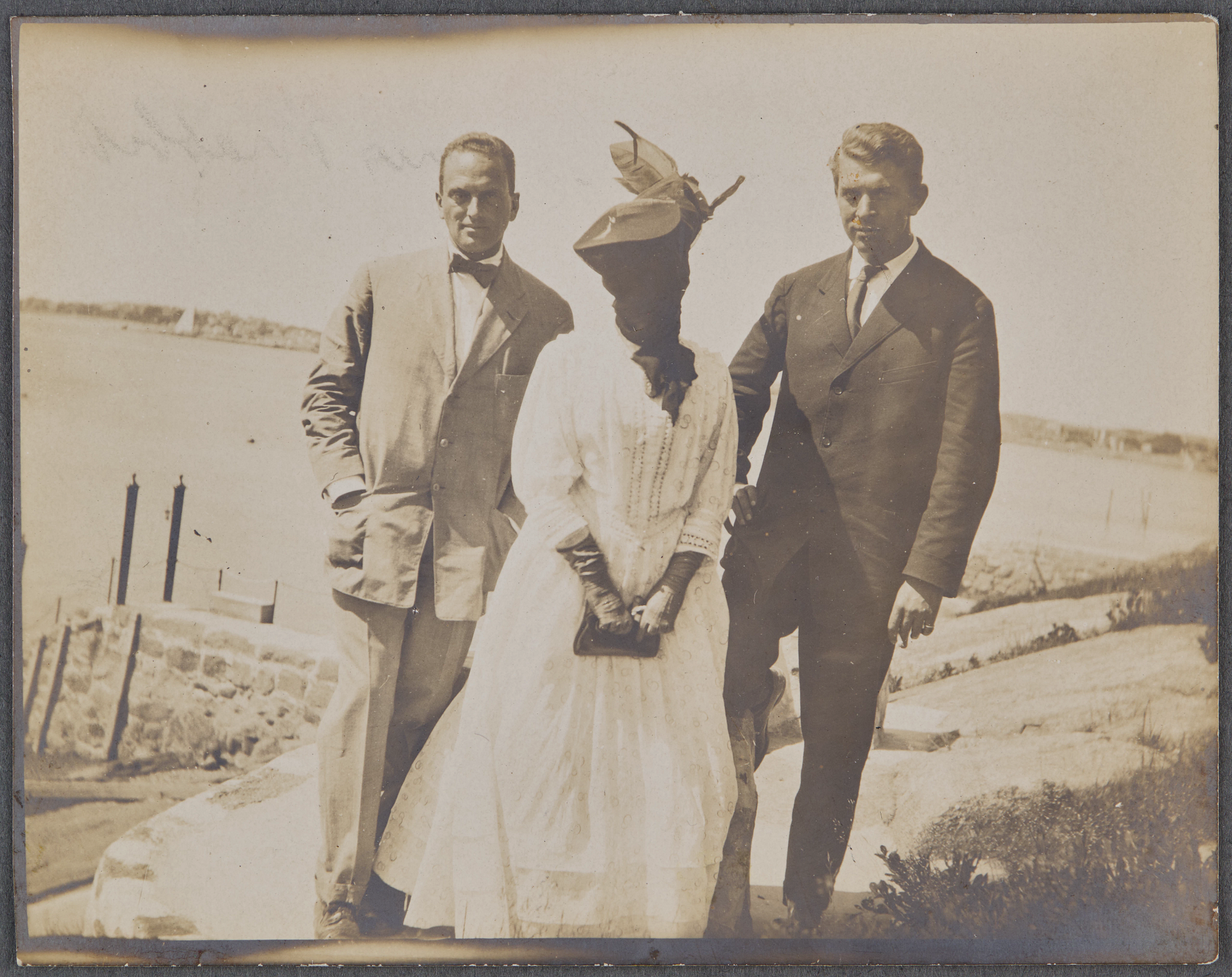 Black and white photo of two men standing next to Isabella Stewart Gardner who has her face covered