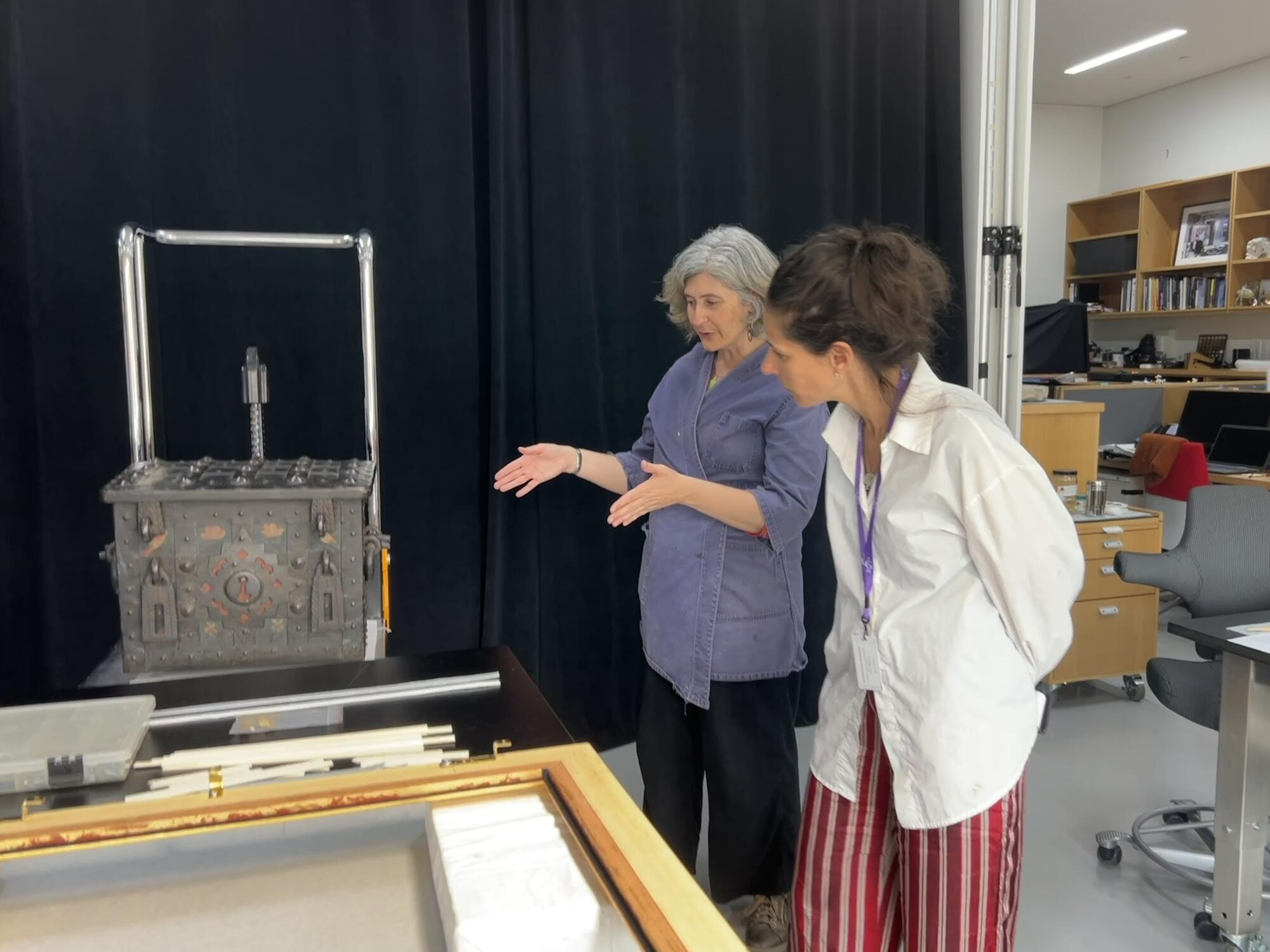 Two women standing in a laboratory space looking at a metal box