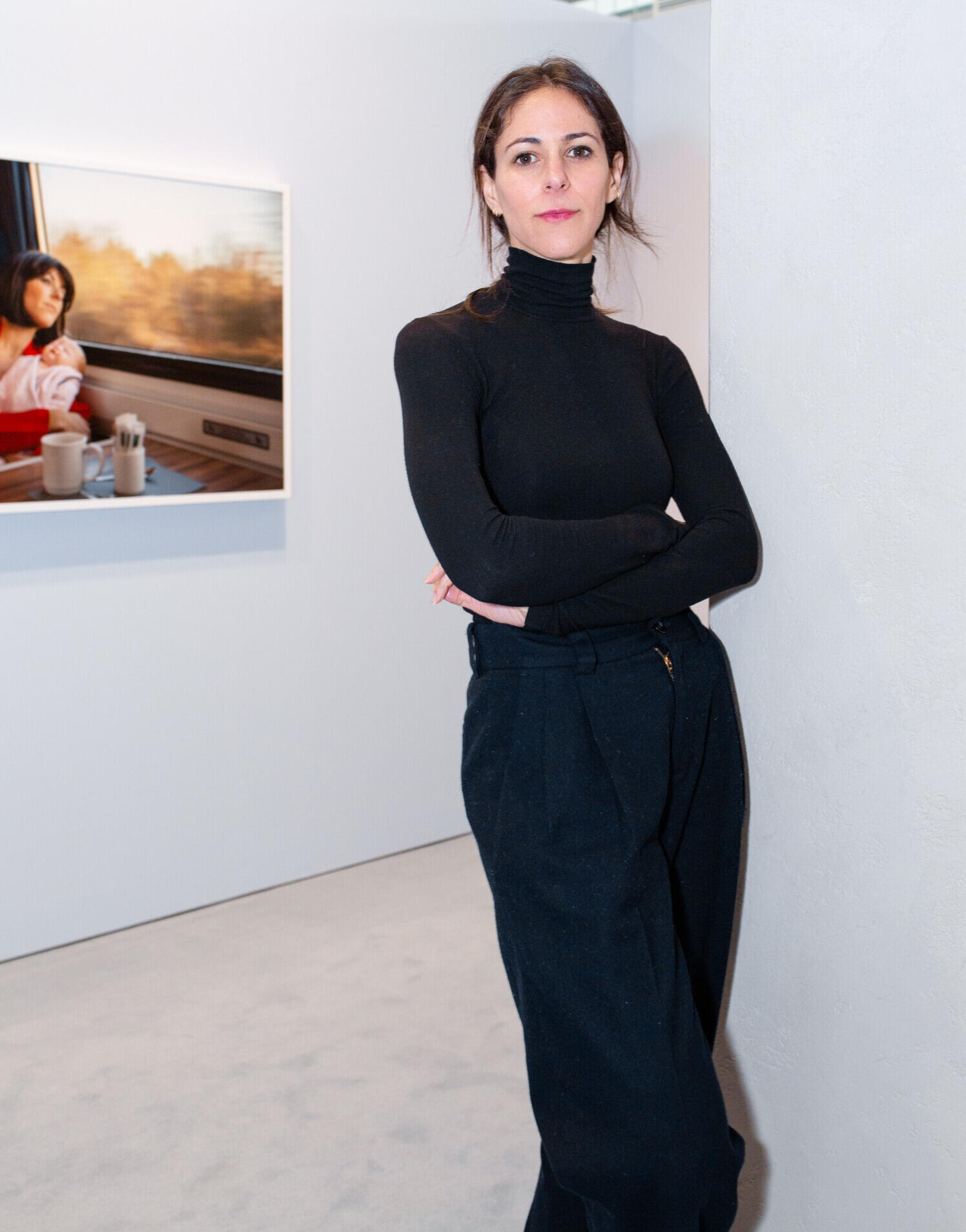 Woman with dark hair wearing slacks and a black turtle neck sweater, standing confidently with her arms crossed across her body. 