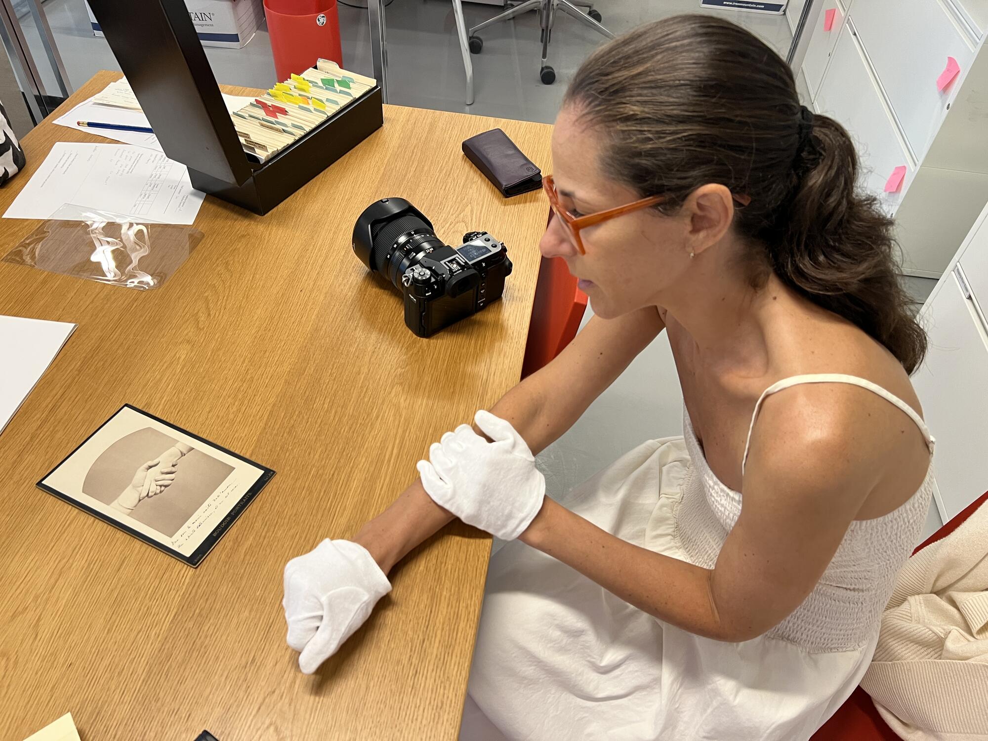 A woman wearing white, loth gloves, examining a photograph of two hands. 
