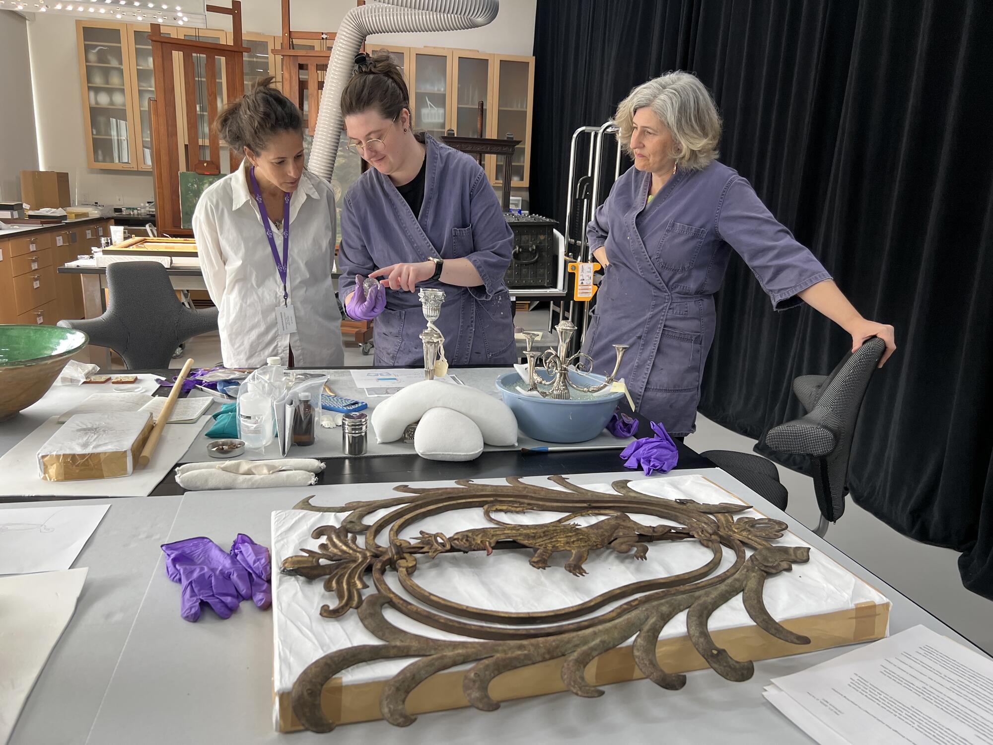 Three women examing candle stickes in a laboratory like setting 