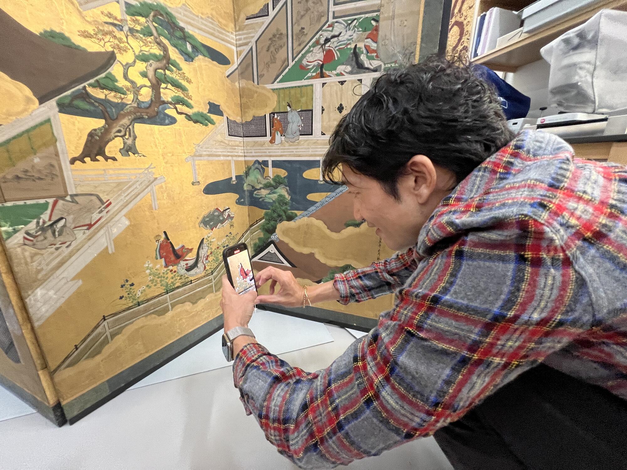 An Asian man at floor level carefully examining a Japanese screen. 