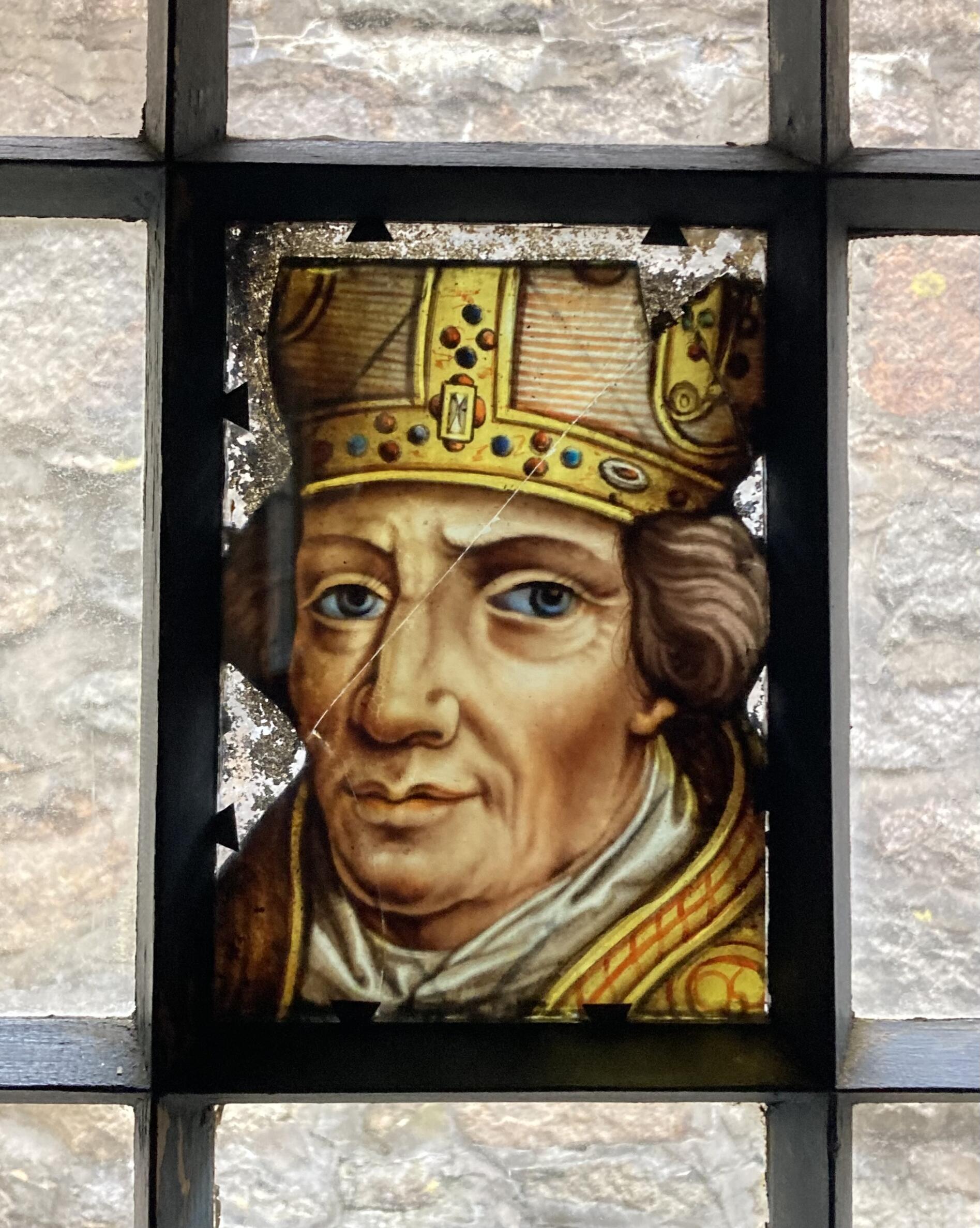 A stained glass pane of a bishop’s head with a lazy eye.