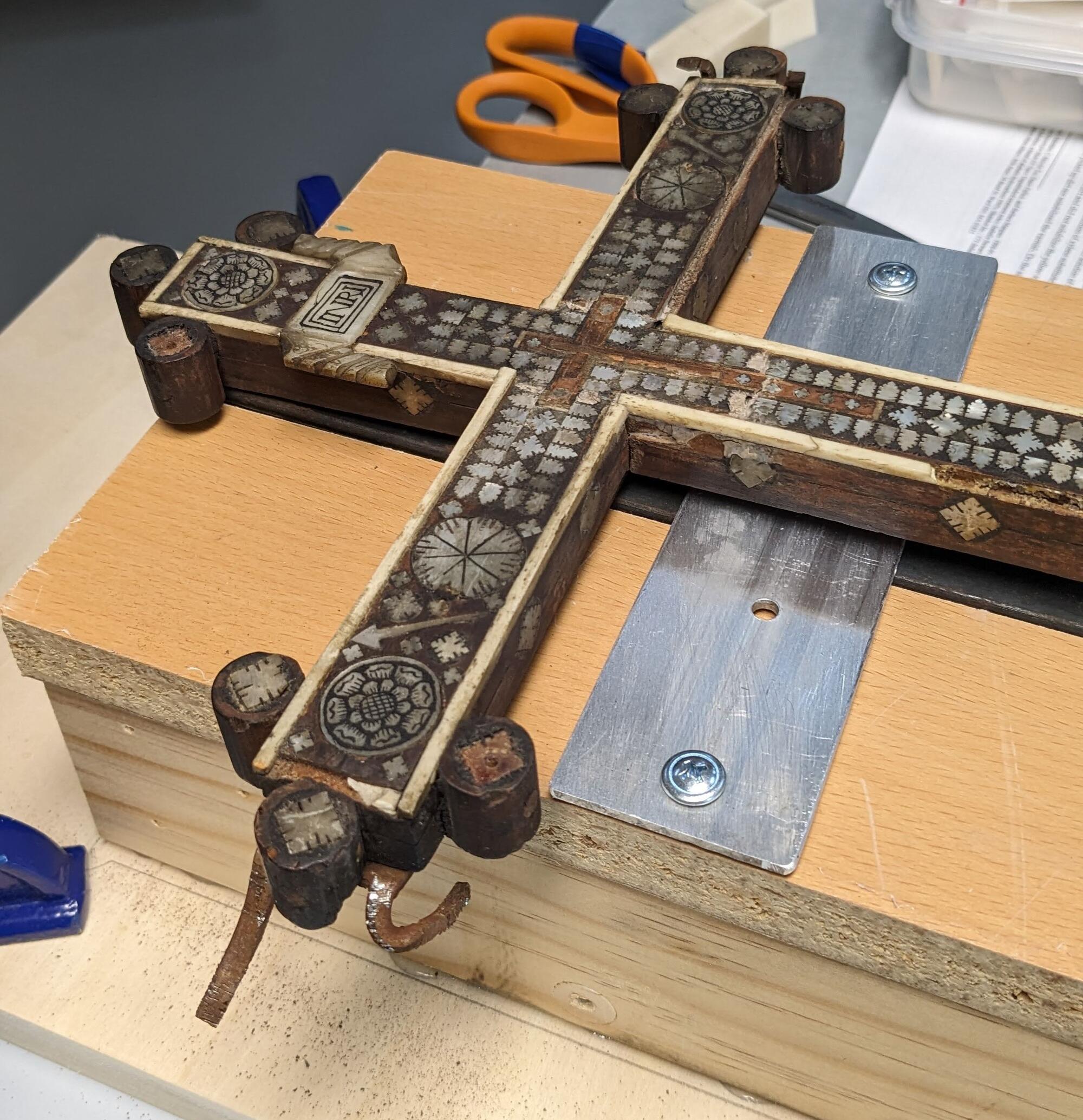 Cross laid down in a custom support to remove the mount. The metal prongs of the mount were pried away from the object. 