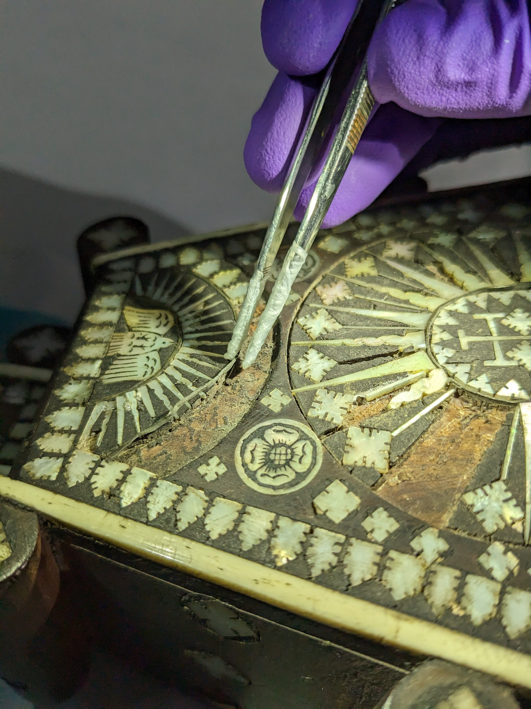 Metal tweezers wrapped in protective film, straightening the metal trim of mother-of-pearl inlays. 