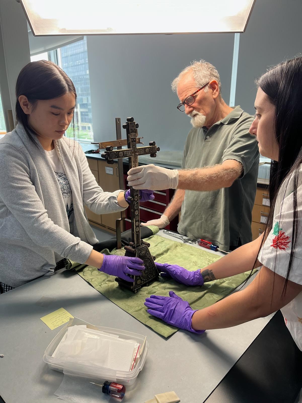 Three colleagues carefully holding the object on the base and cross to remove it from the mount. 