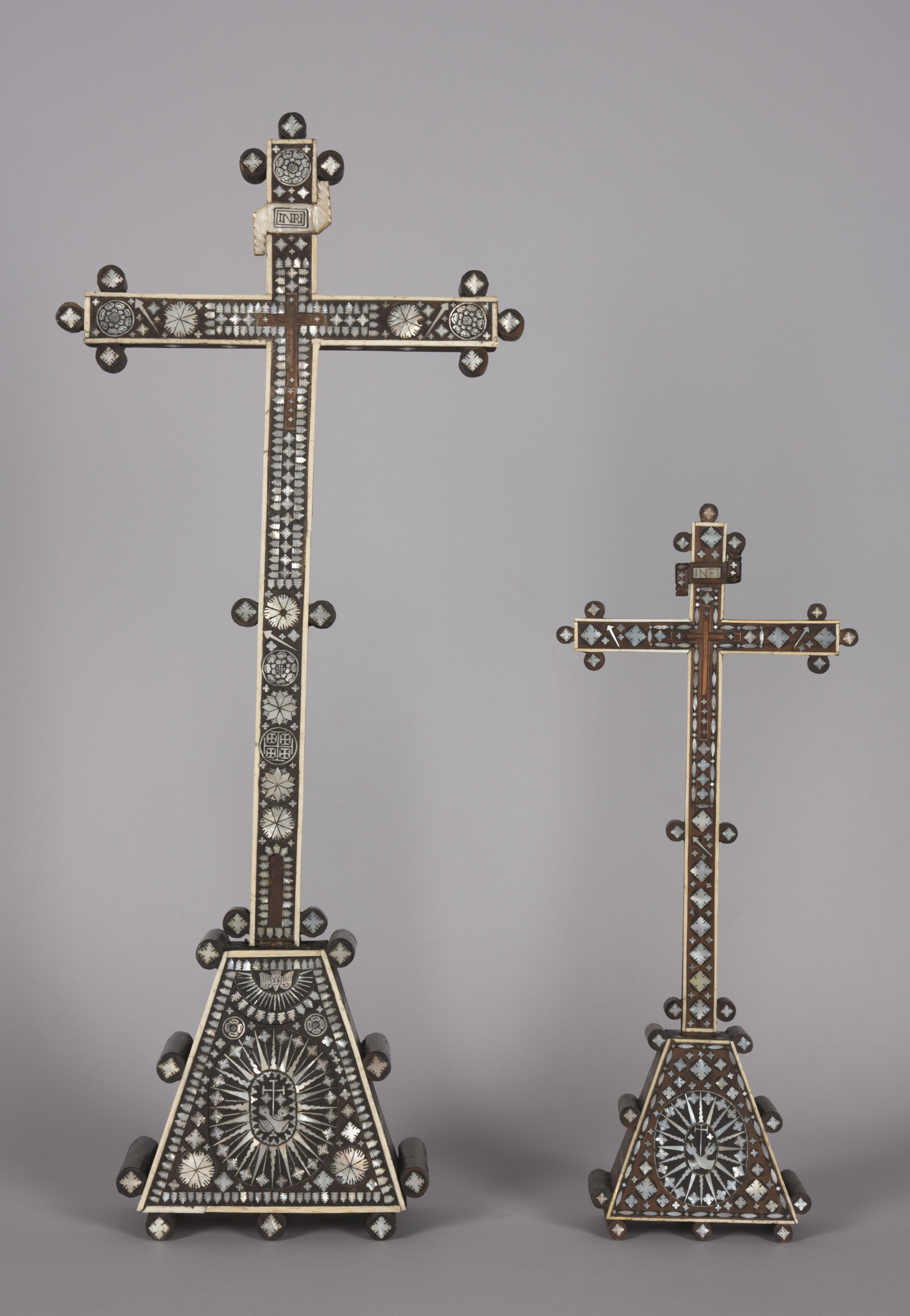 wo wooden crosses, inlaid with mother-of-pearl, are next to each other. The left cross is slightly larger and more ornately decorated than the one on the right but both are very stylistically similar. 