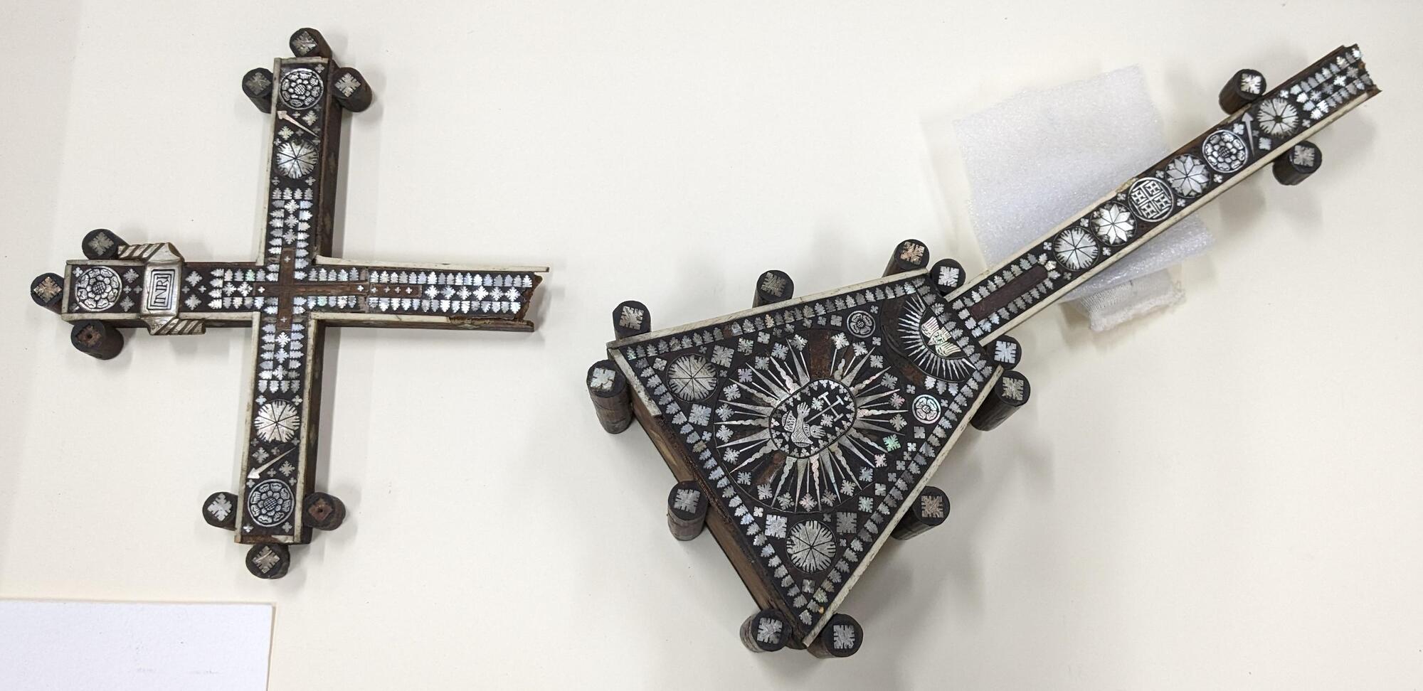 Object laid down on a white background in two fragments, broken horizontally in the middle of the cross.