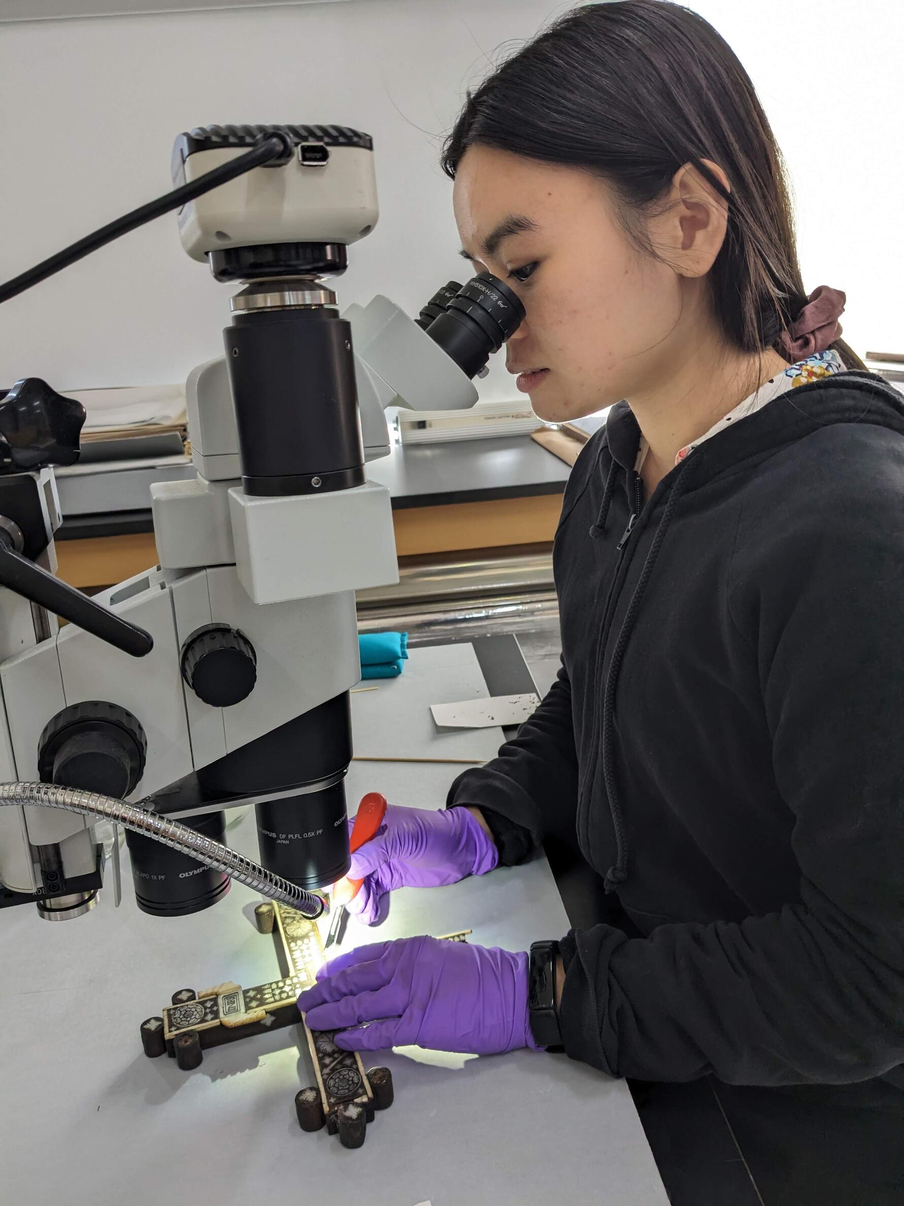  The top half of the cross is underneath a stereo microscope while a conservator removes old adhesive with a scalpel. 