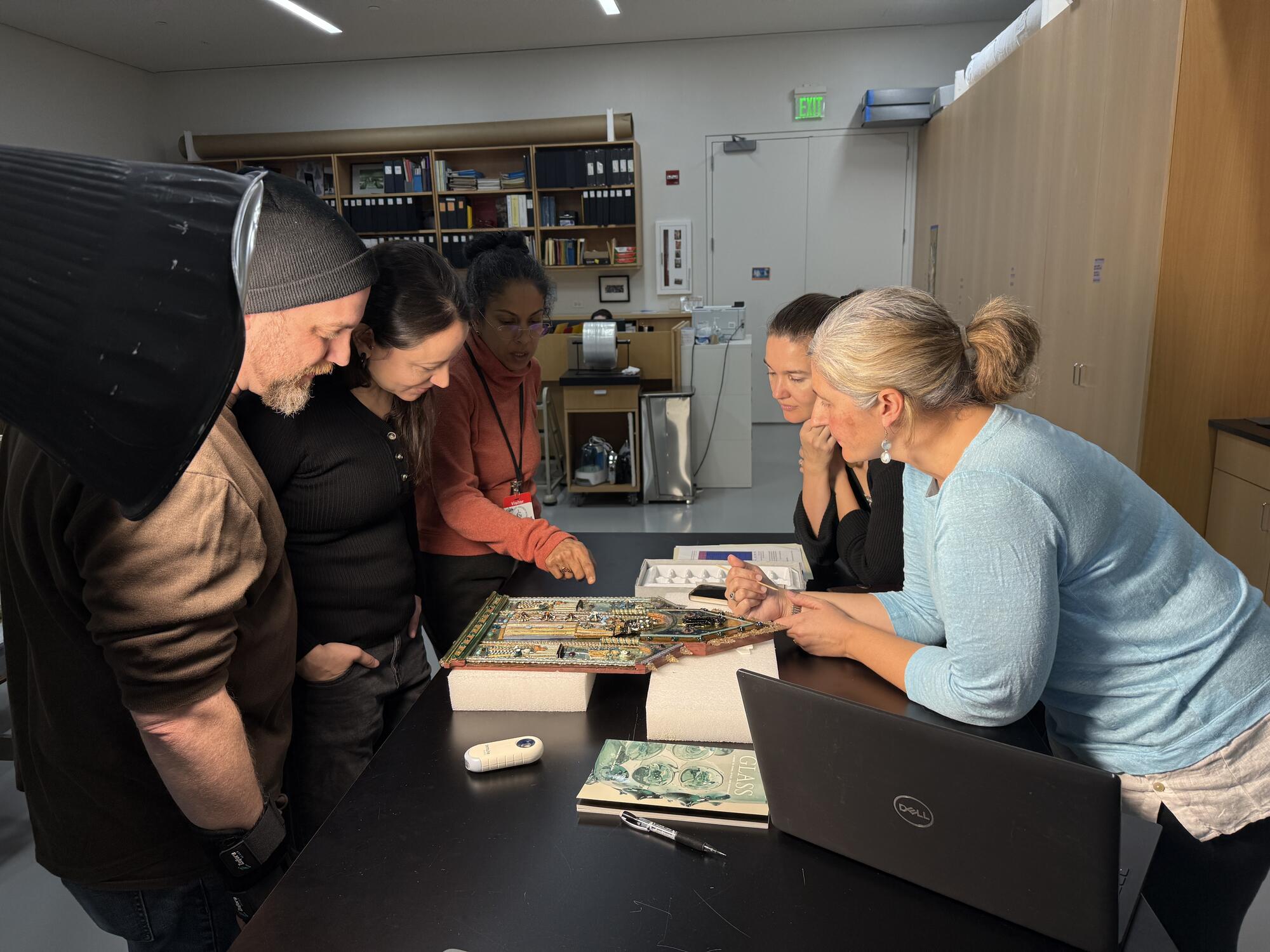 Five people stand around a table examining the Black Glass Madonna. One person points at a part of the sculpture.  