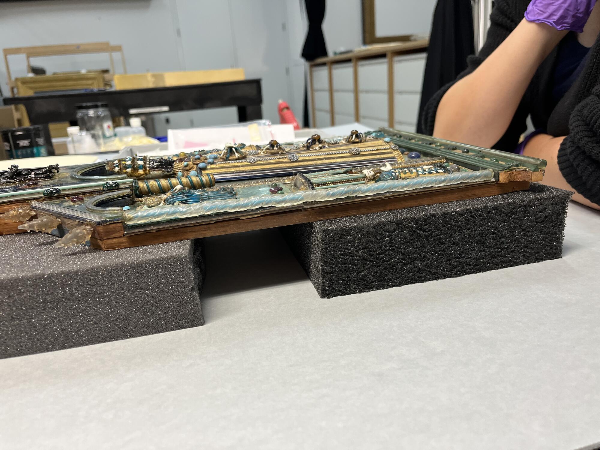 Side view of the sculpture showing the layered structure of wood, paper and multi-colored glass elements.