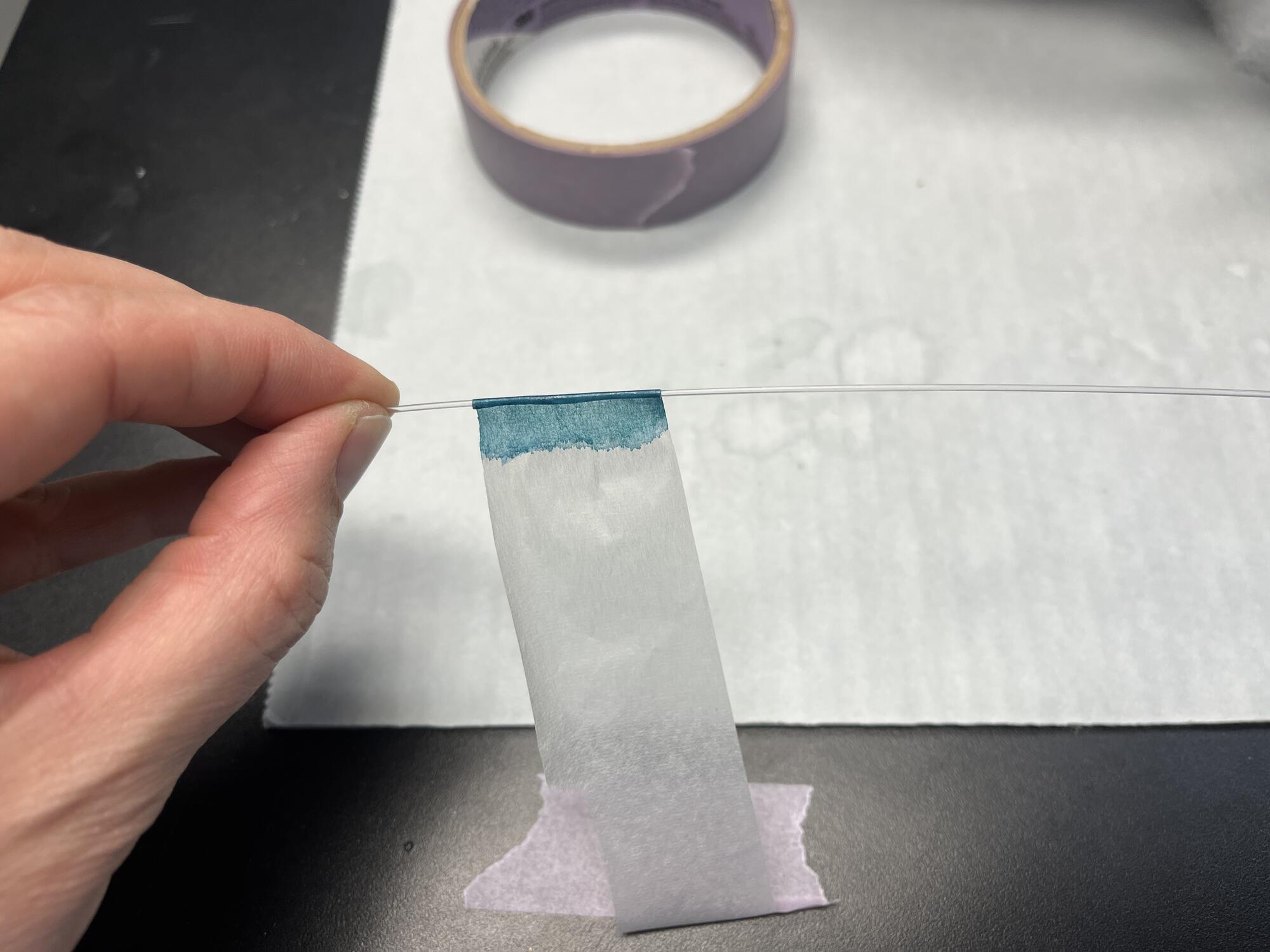 Detail of a conservator’s hands rolling the turquoise painted paper around the thin acrylic rod.