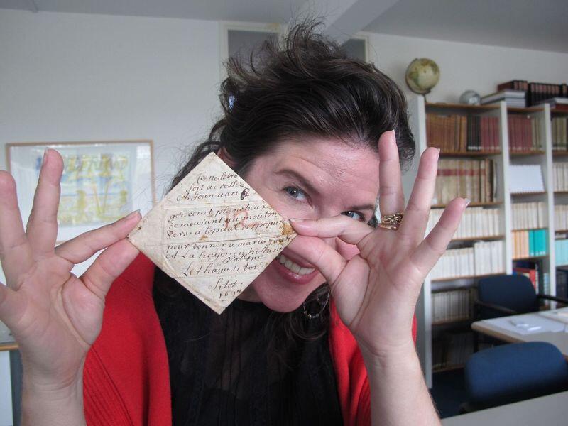 A woman holding up a folded envelope, smiling directly at the camera. 