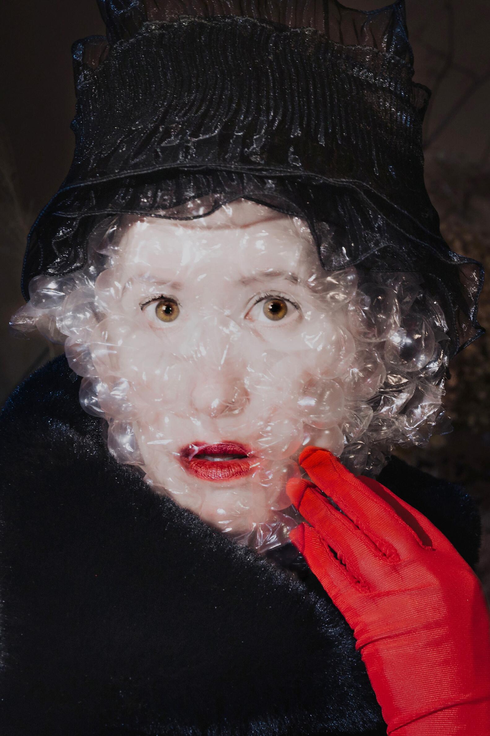 woman with red glove, red lipstick, black lace hat with bubble wrap over her face