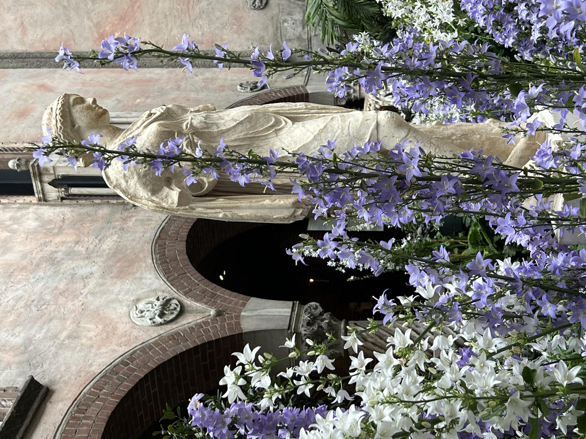 A statue of the Goddess Artemis surrounded by flowers.