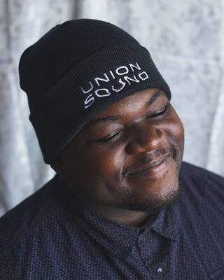 headshot of man in black beanie smiling and looking down