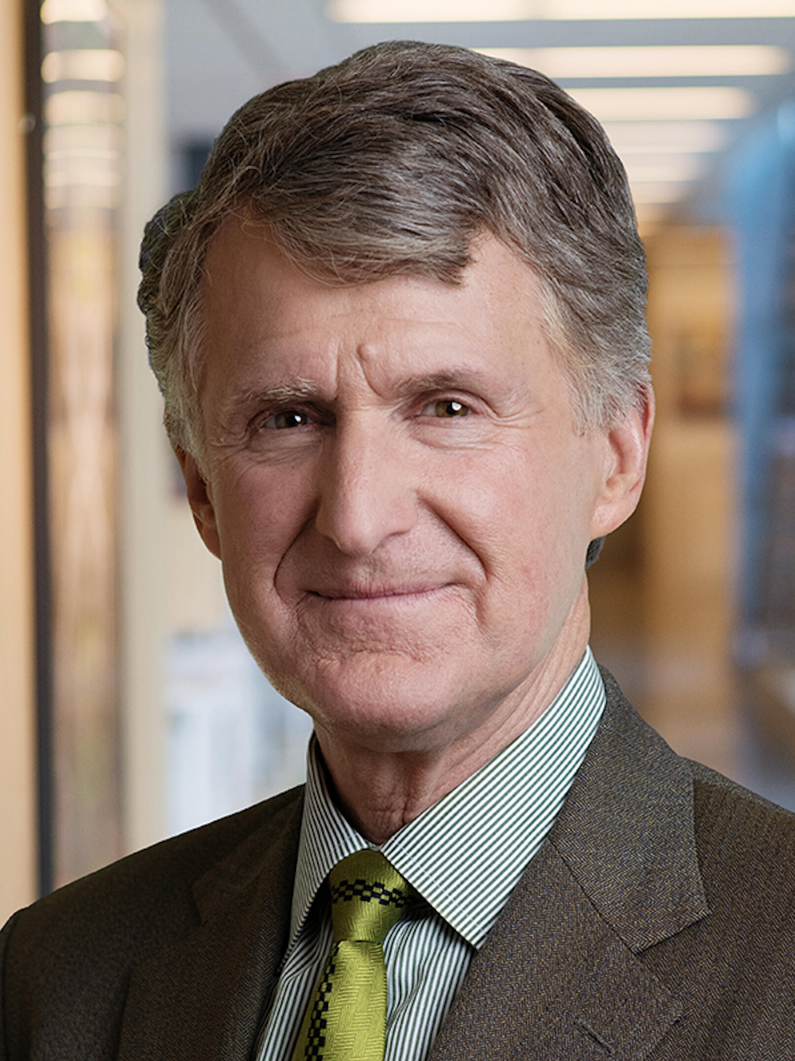 Headshot of a man with greying hair in a suit and tie looking directly at the camera. 