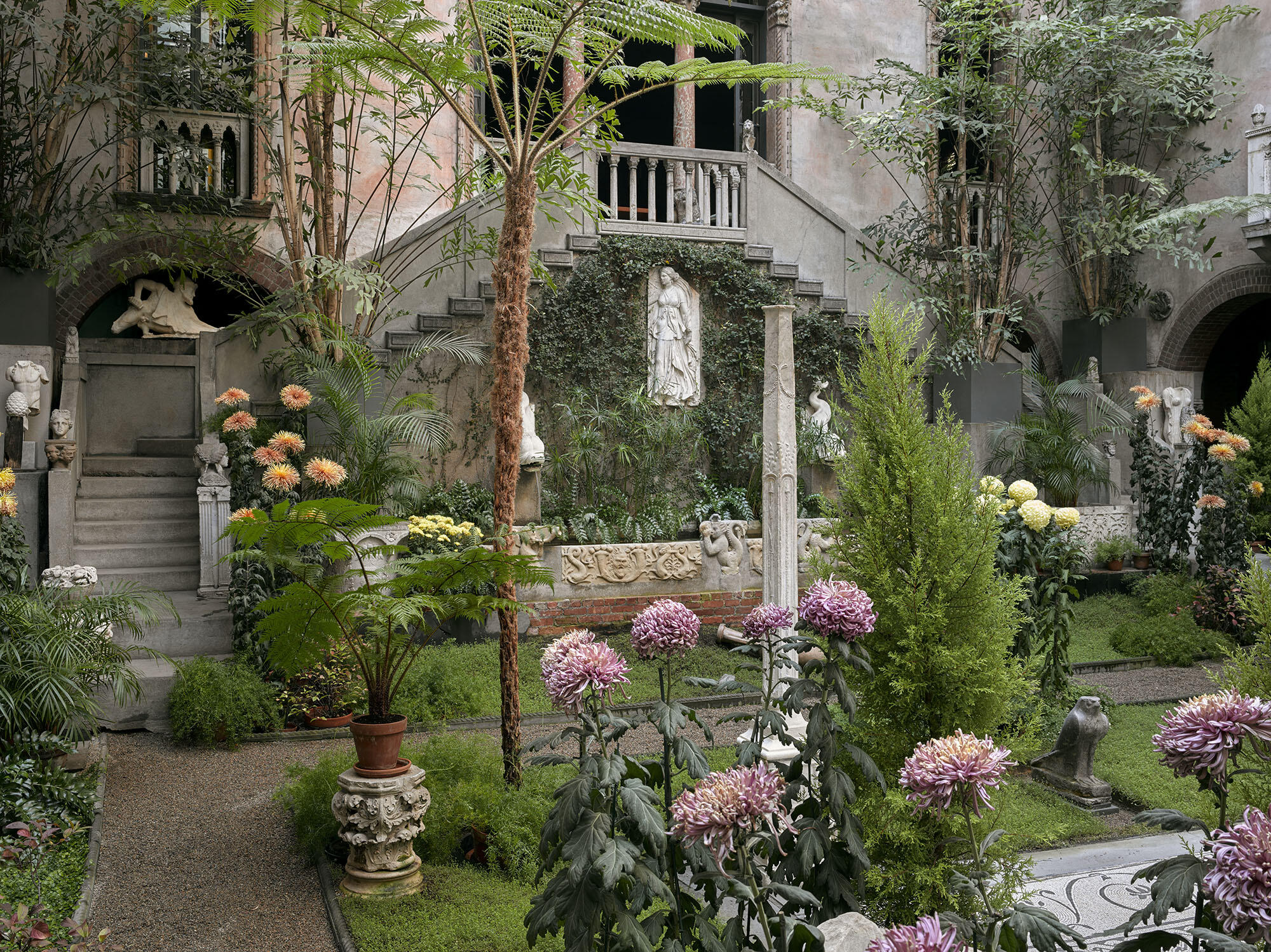 A garden courtyard filled with flowers and Roman sculpture.