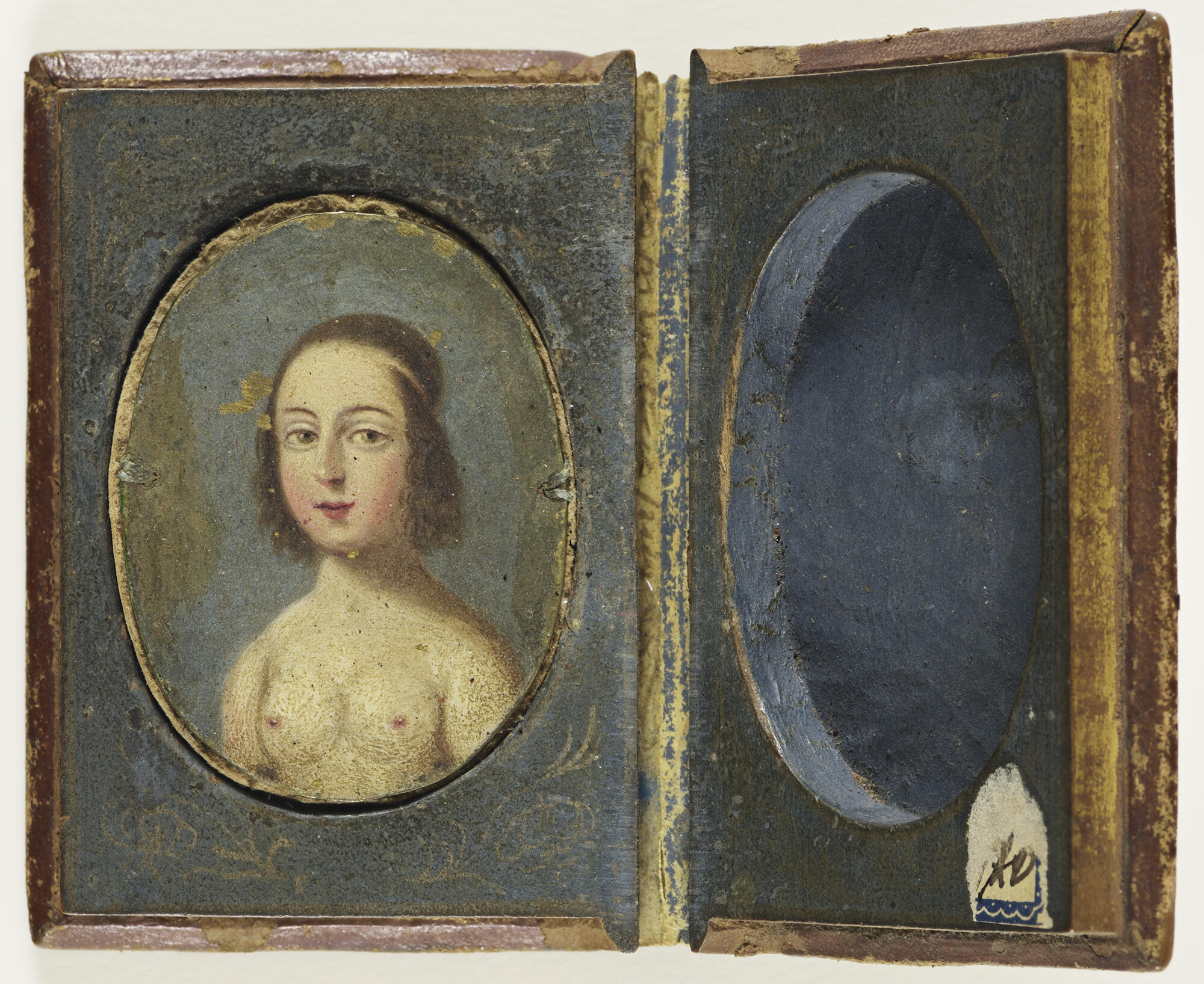 An open case with a painted bust of nude woman on the left. She has a long oval face, straight nose, hazel eyes, and rosy cheeks.