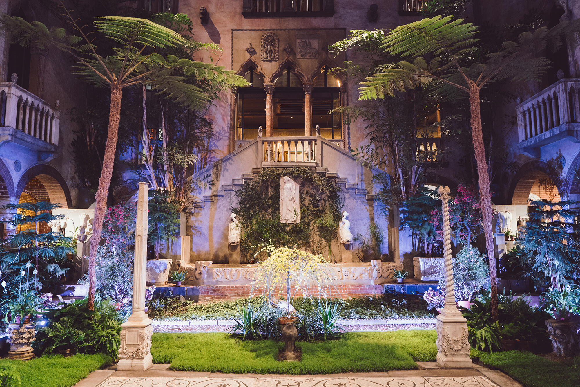 A garden courtyard illuminated at night with a balcony and stairs.