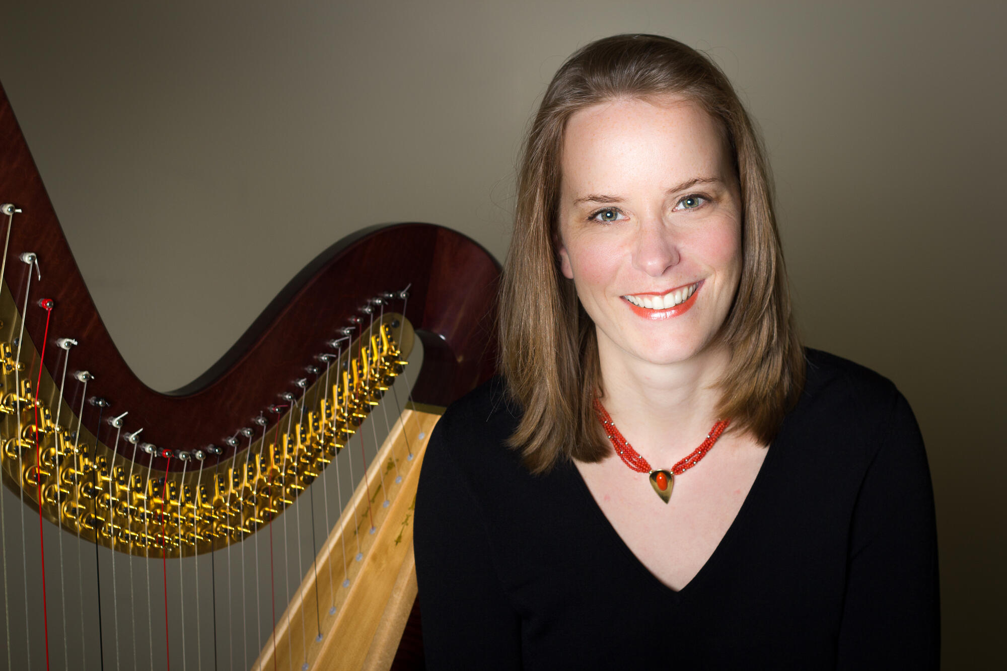 Woman sitting next to a harp wearing an orange necklace and black sweater