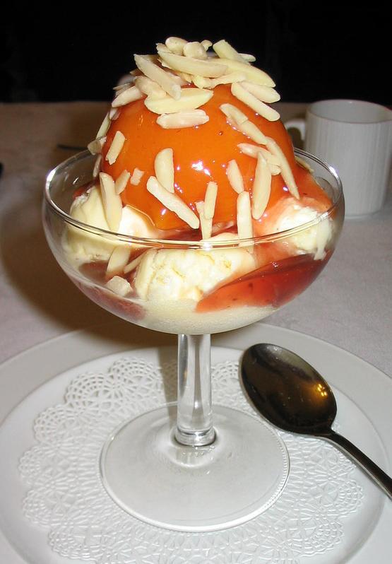 A dessert of peaches and raspberry sauce with vanilla ice cream in a glass dish.