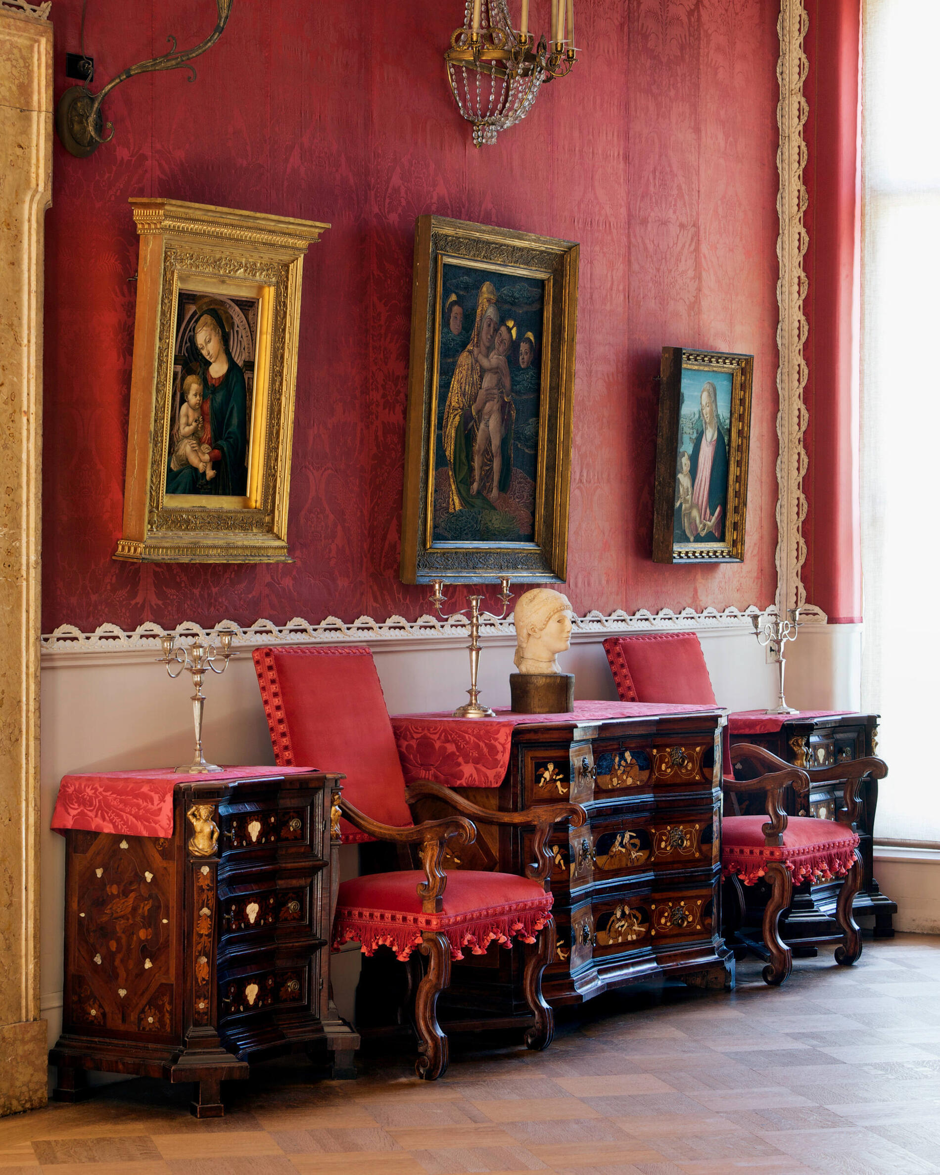 A gallery with three paintings of mothers and babies and red upholstered walls.