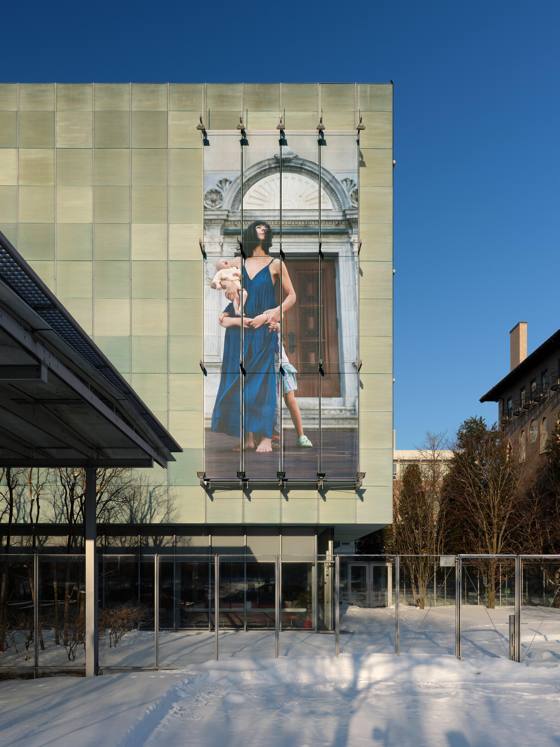 A large photographic installation of a woman holding a baby while arms of two children encircle her from behind.