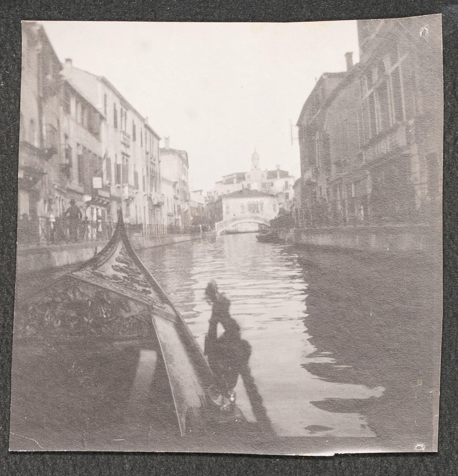 A black and white photograph of the tip of a gondola in a Venetian canal.