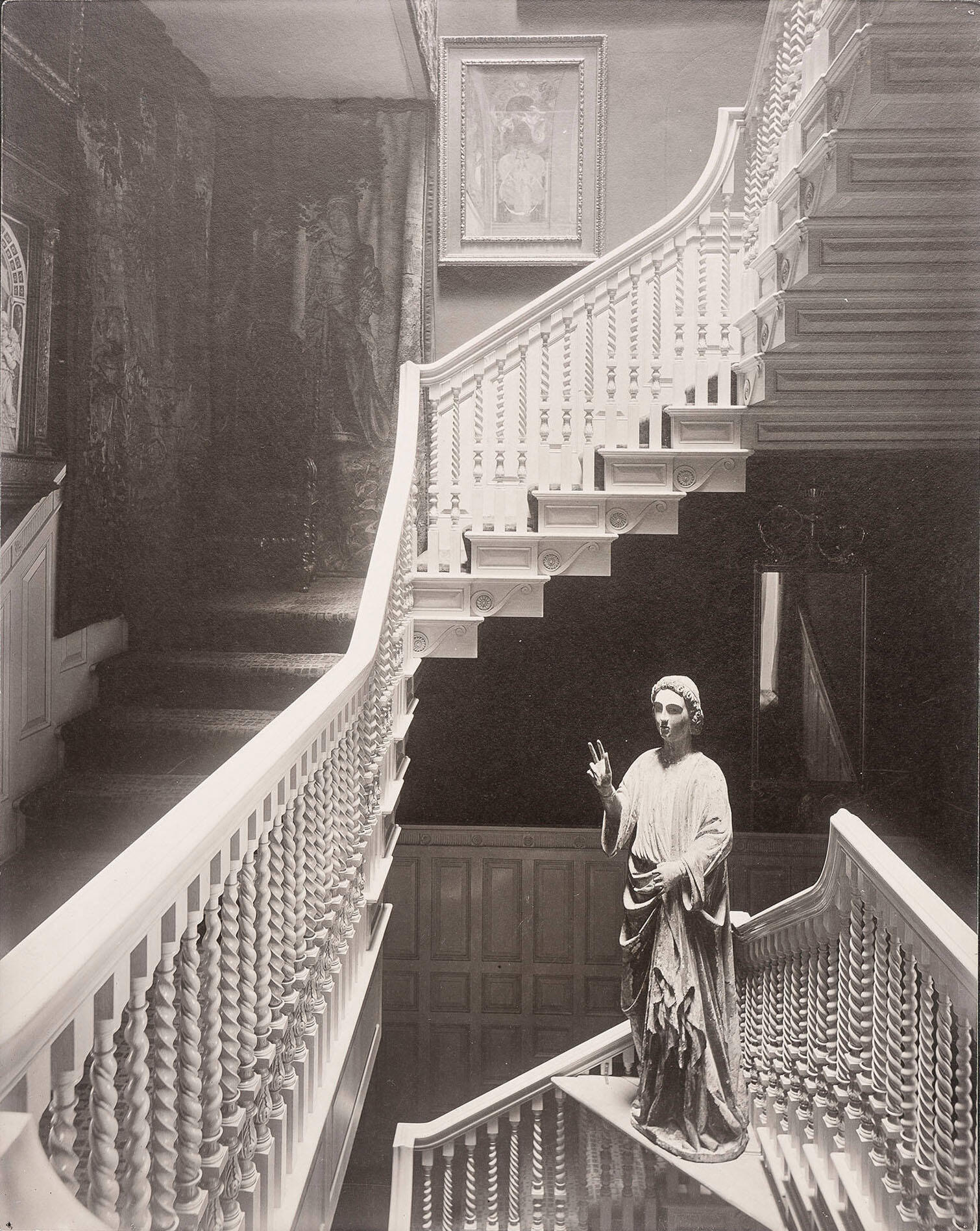 A black and white photograph of a stairwell with white carved balusters.