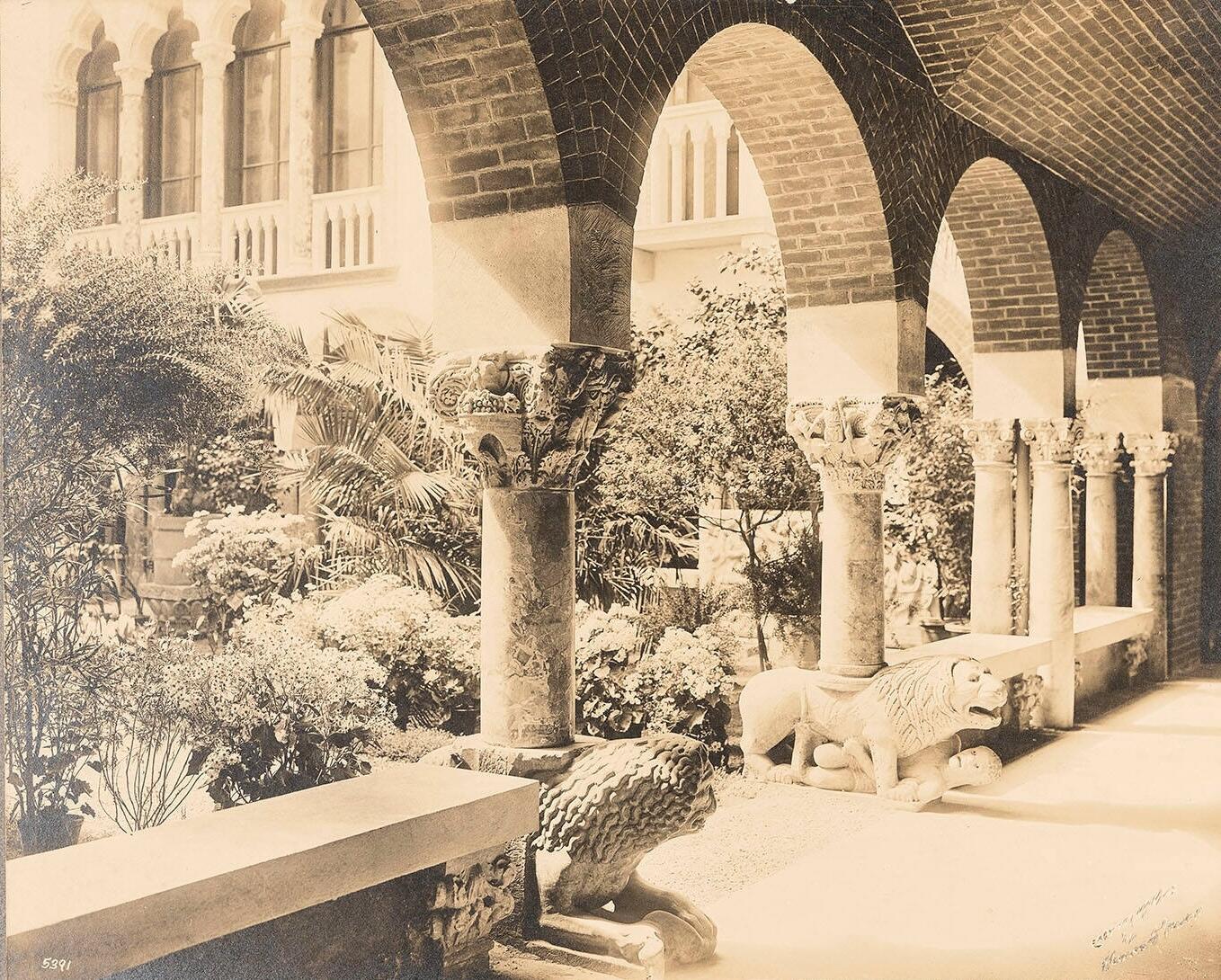 A black and white photograph of an arched cloister looking into a garden courtyard