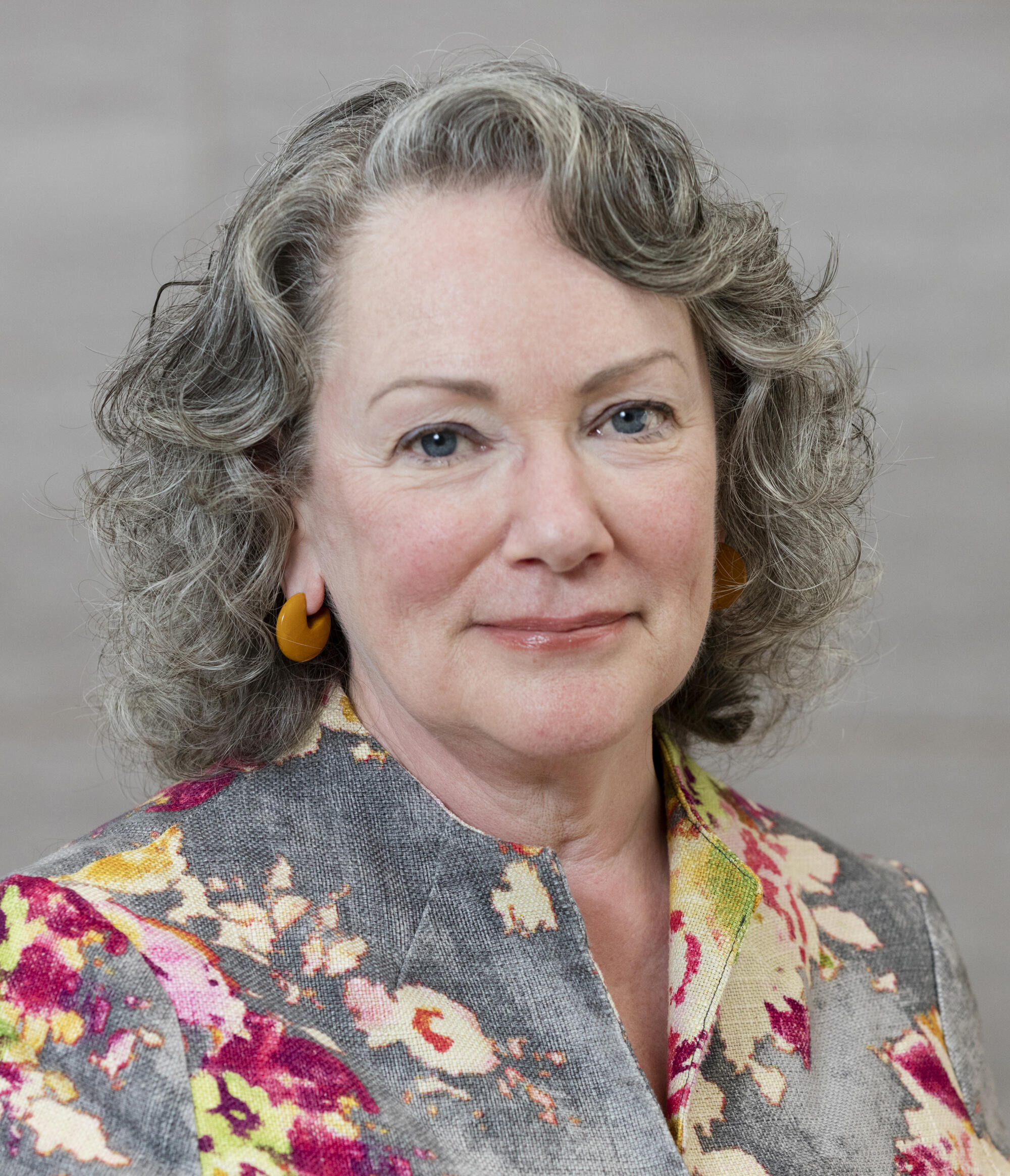 Headshot of woman with gray curly hair and a floral top