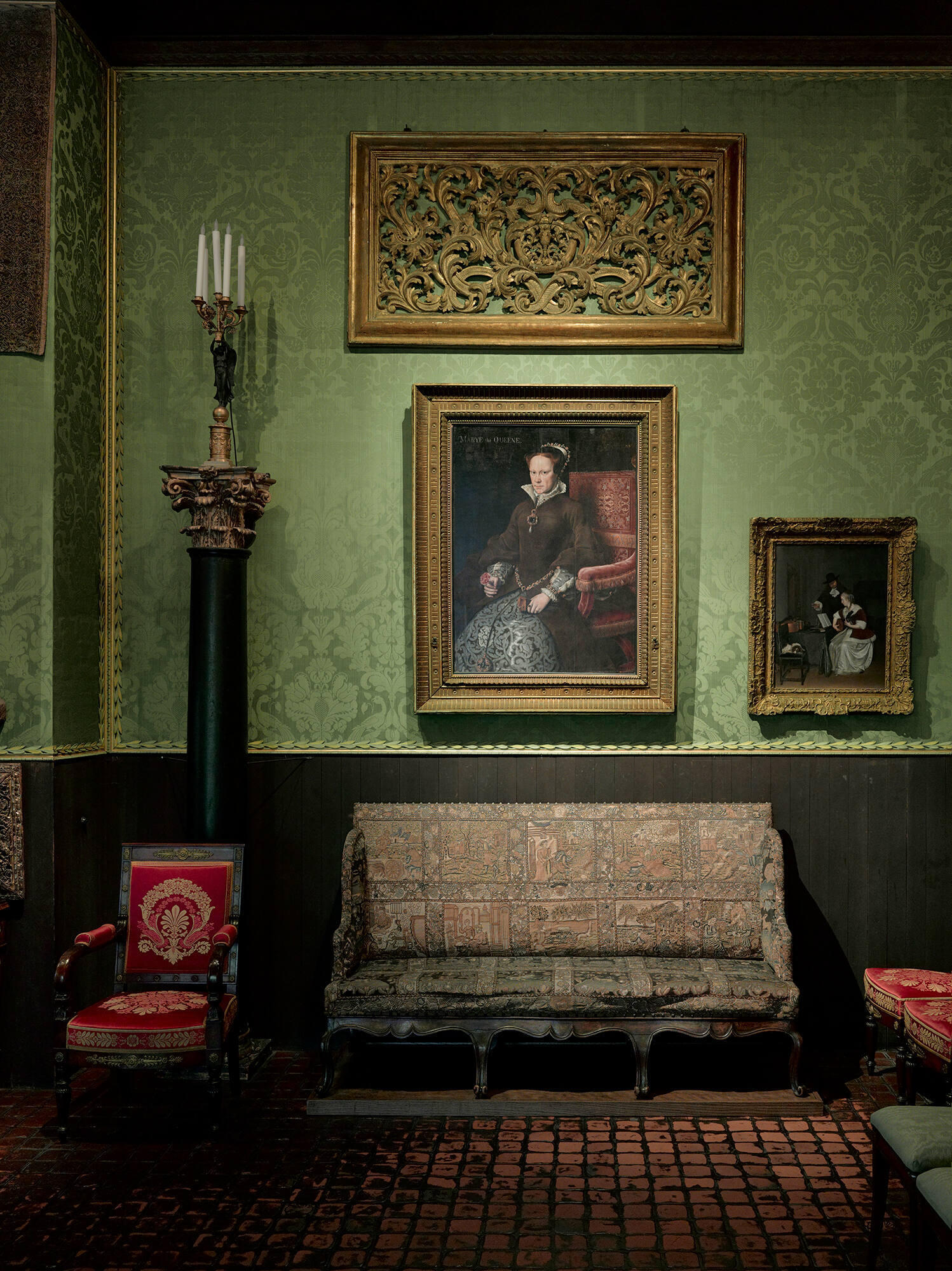 A small sofa with embroidered upholstery in a room with green upholstered walls.