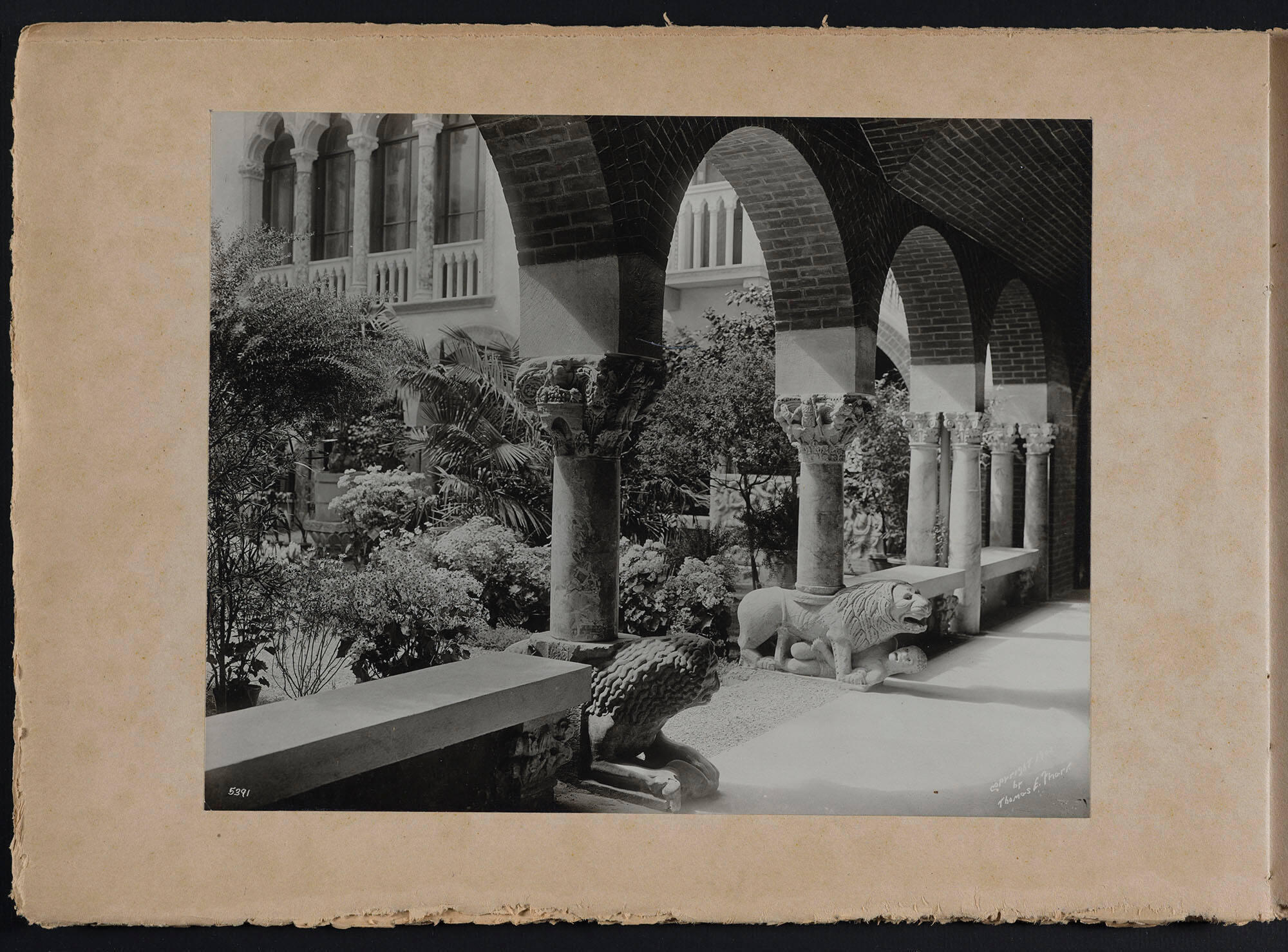 A black and white photograph of an arched cloister looking into a garden courtyard.