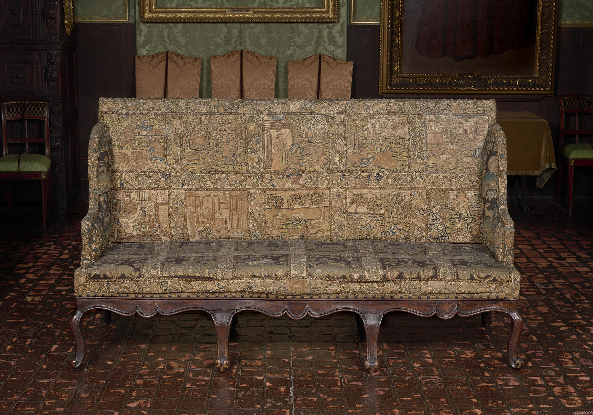 A high-backed sofa with embroidered upholstery. The seat is uneven.