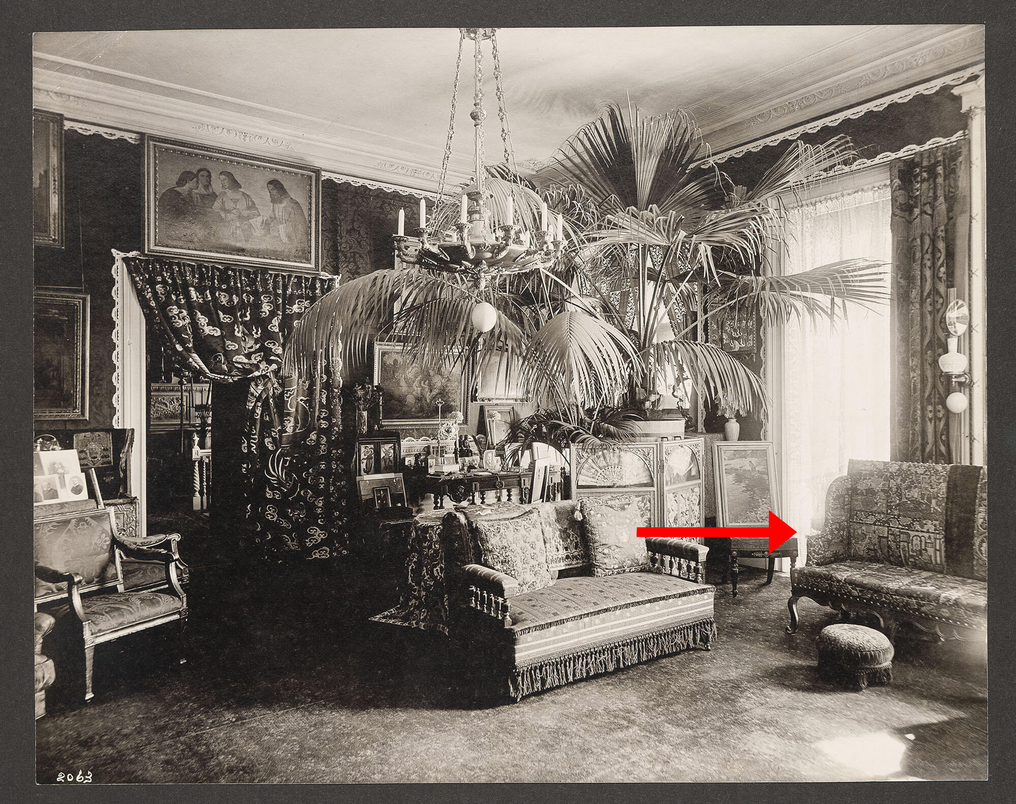 A black and white photograph of Isabella’s densely furnished Drawing Room with an arrow pointing to the sofa.