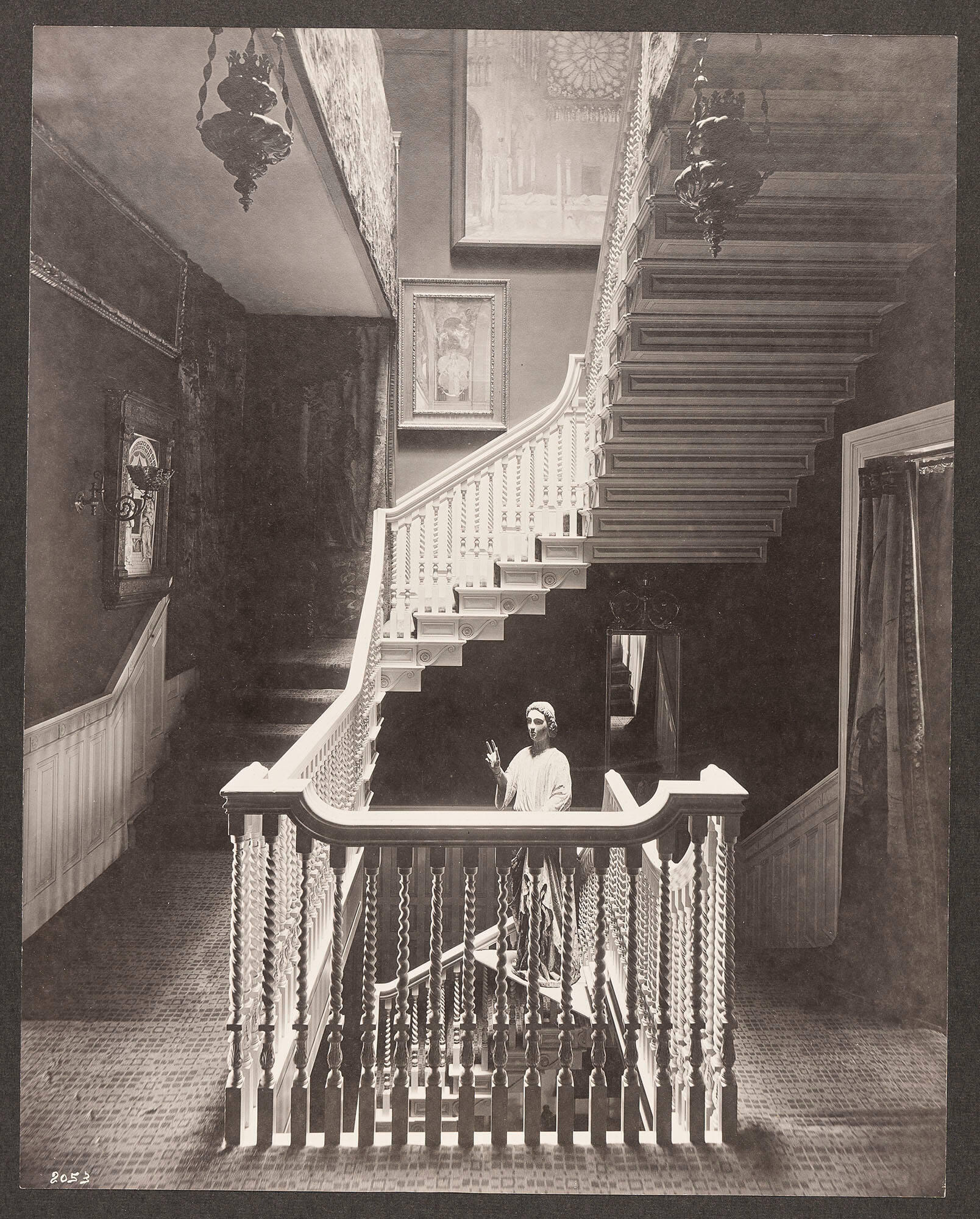 A black and white photograph of a stairway with a painting of the interior of a cathedral with a large rose window over a smaller painting of an architectural interior.