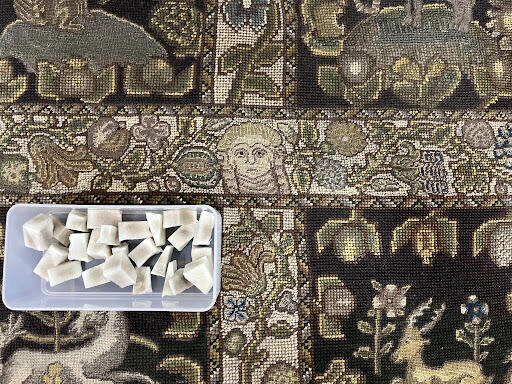 A plastic bin of cosmetic sponges sits on top of the embroidered seat of the sofa.